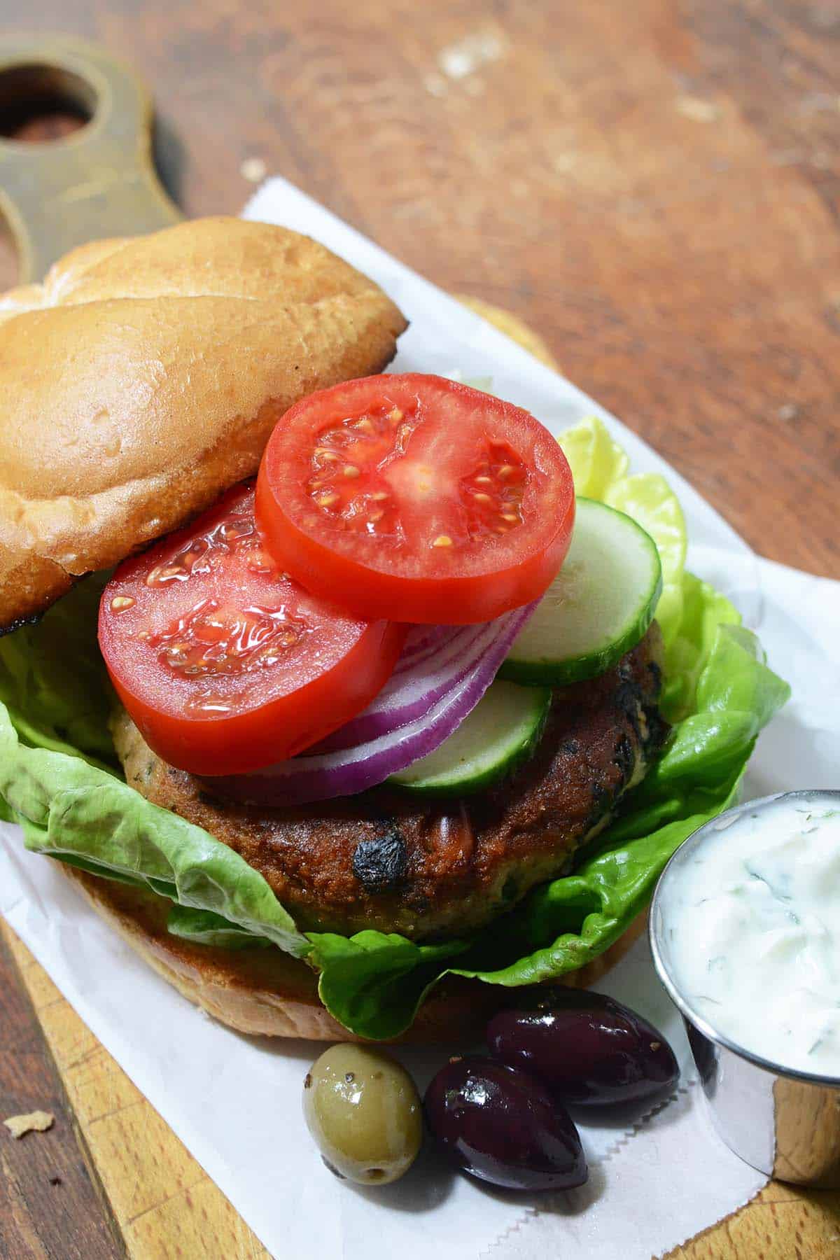 front view of turkey burger with feta and pine nuts on bun with tomato and cucumber