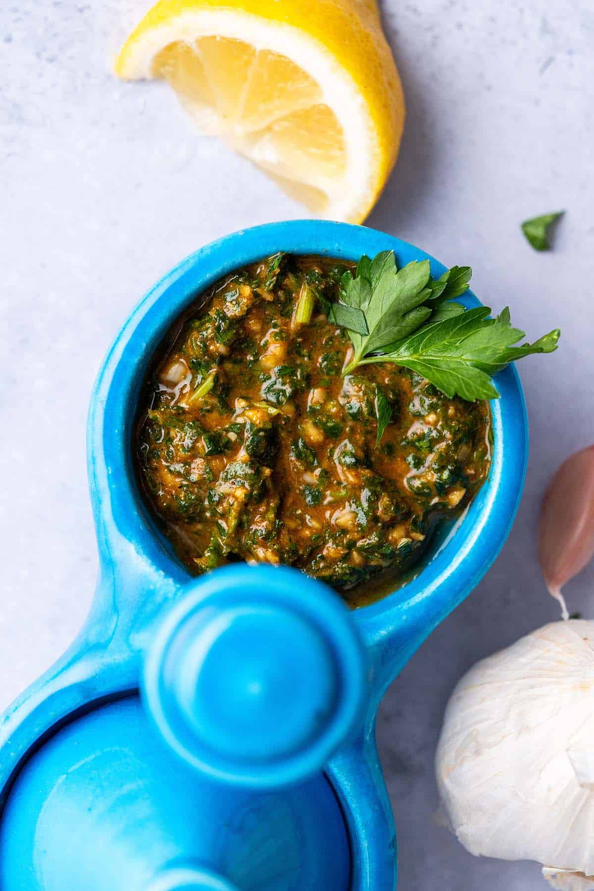 overhead view of chermoula sauce in small condiment container with fresh lemon and garlic around