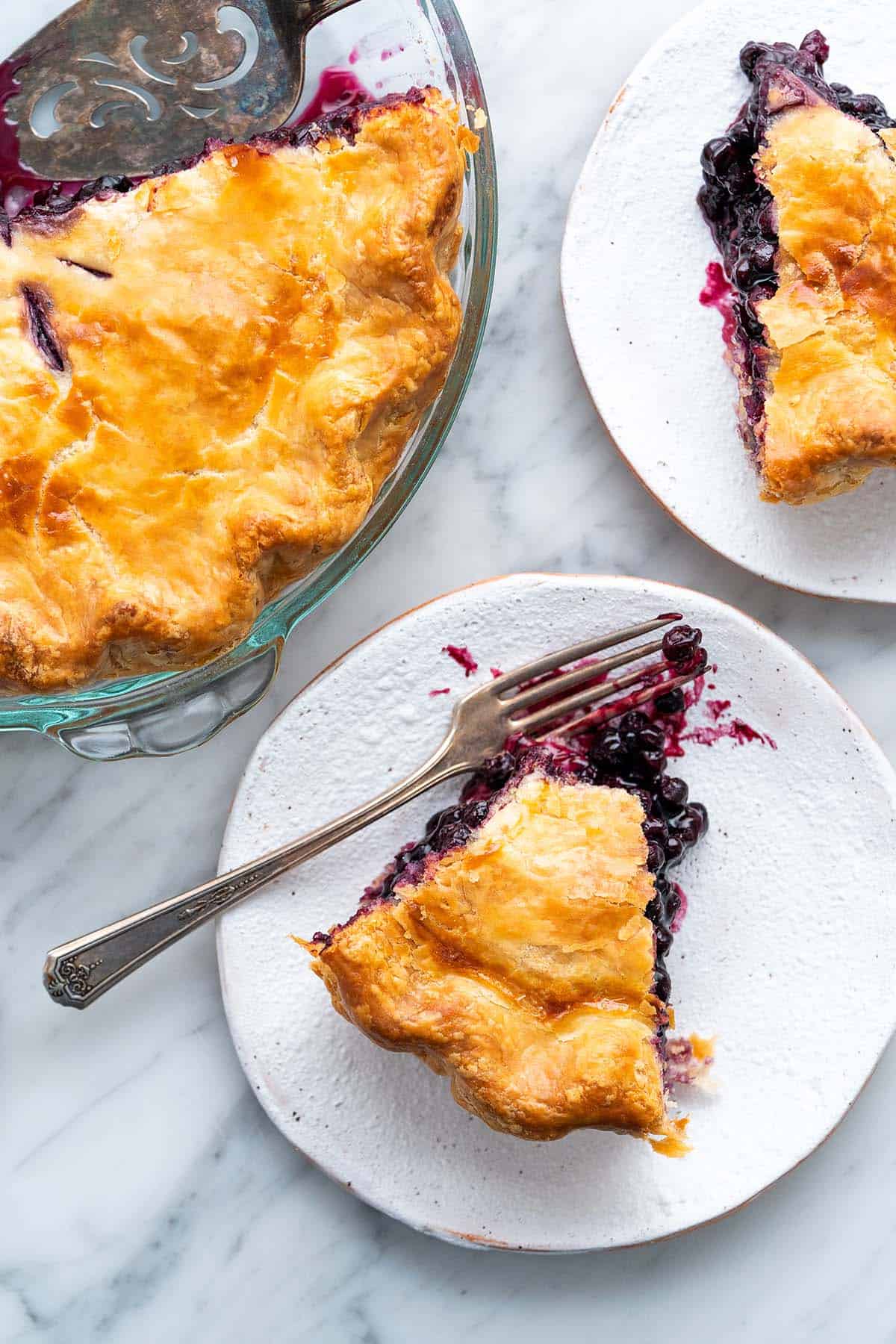 top view of blueberry pie slices with whole pie in photo