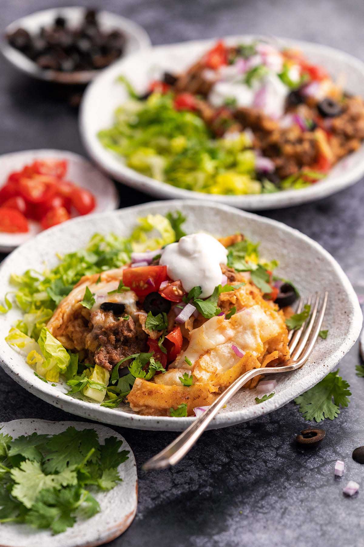beef enchilada casserole with fresh toppings in stoneware dishes