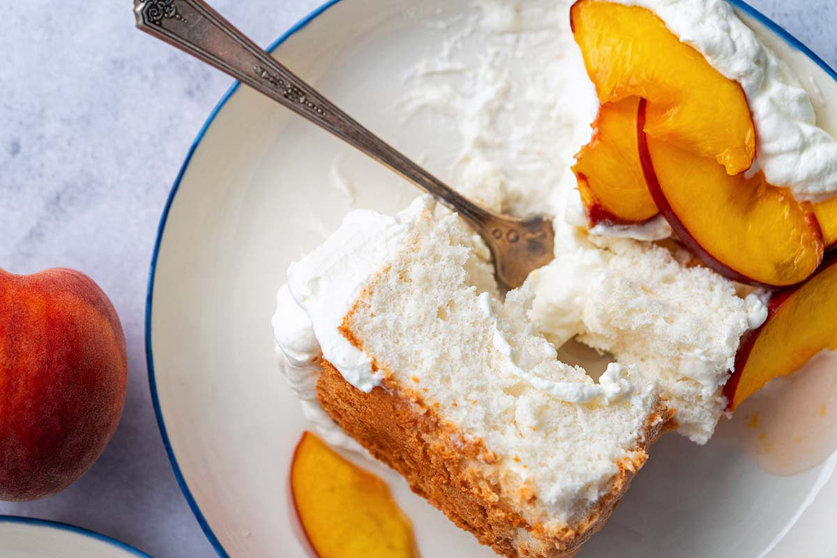 close up of plate with partially eaten piece of angel food cake with whipped cream and fresh peach sauce topping