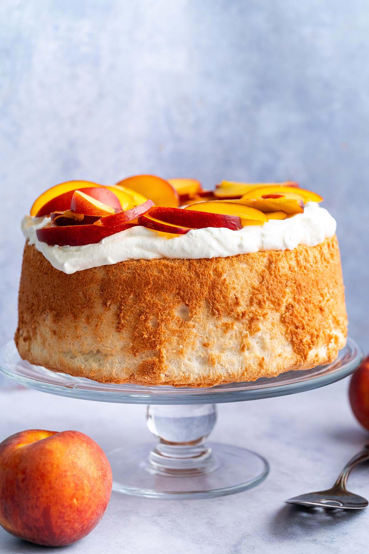 front view of angel food cake with whipped cream and fruit on glass stand