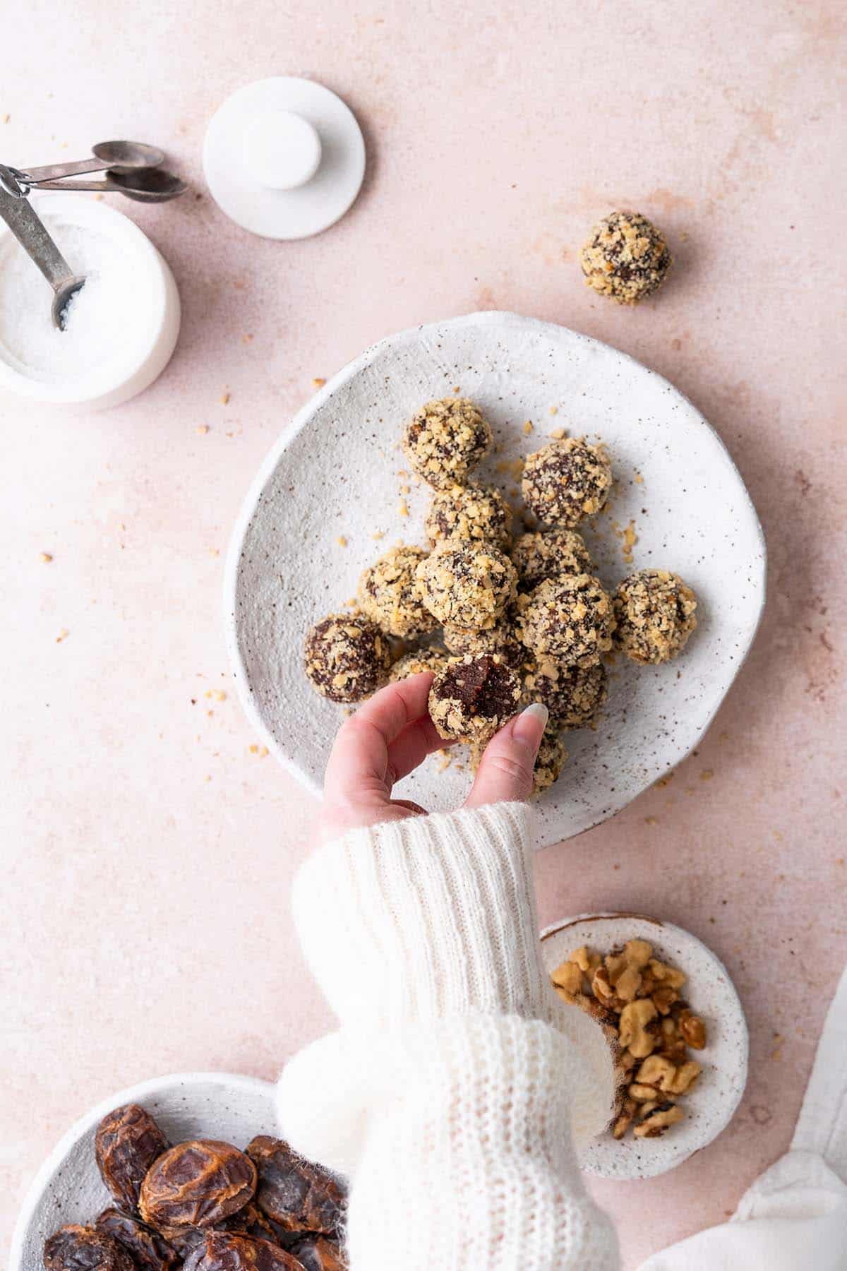 hand reaching in to grab chocolate truffle off plate of date energy balls