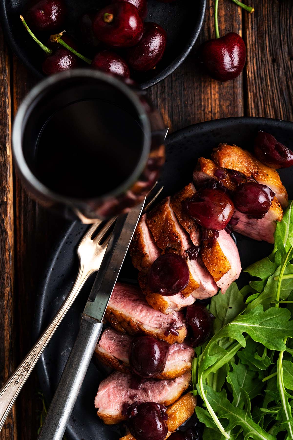 overhead view of duck breast recipe with red wine cherry sauce on plate with salad