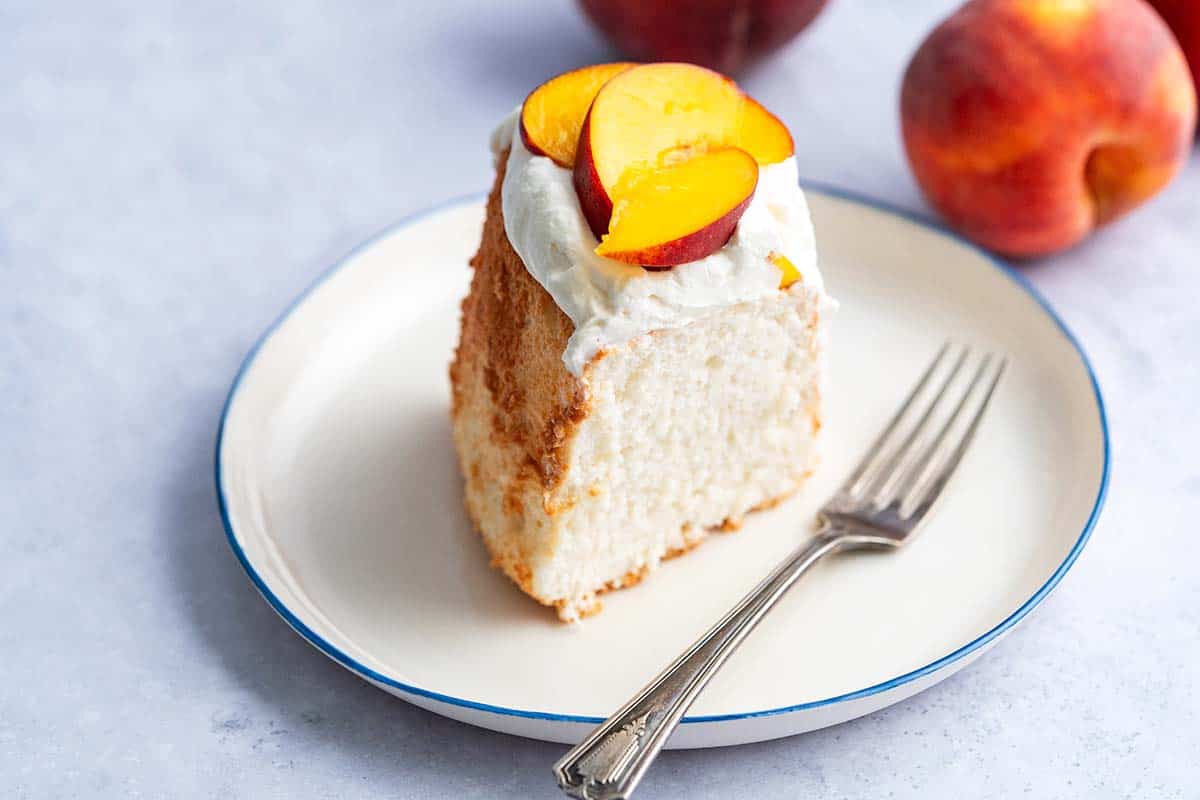 serving of angel food cake on plate topped with whipped cream and fresh peach sauce