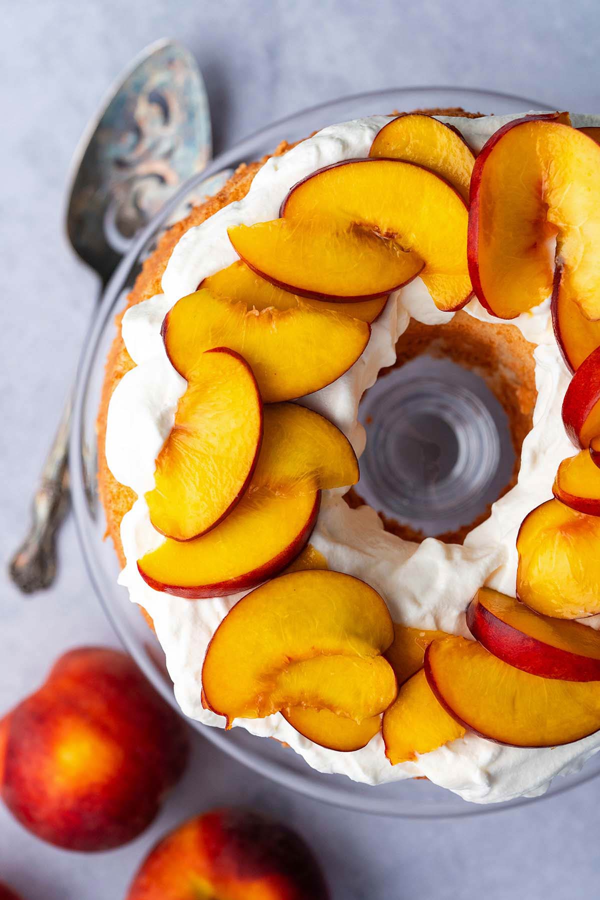 top view of angel cake topped with fresh whipped cream and peach slices