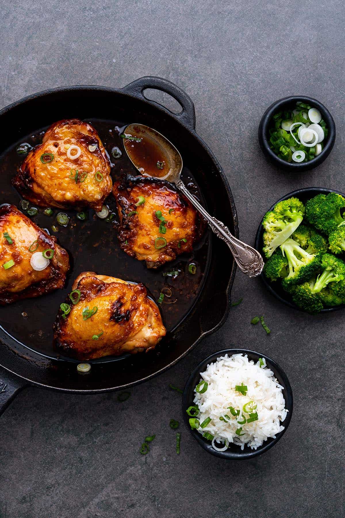 easy honey garlic chicken recipe in cast iron skillet with sides of rice and broccoli