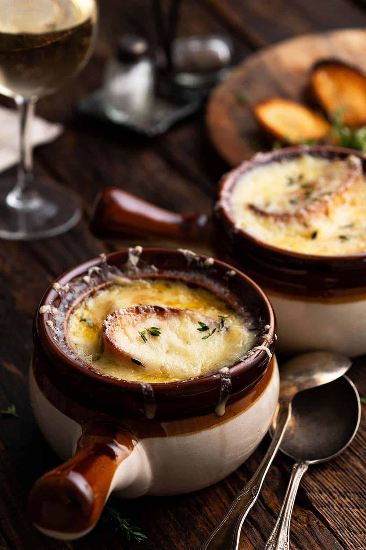 front view of french onion soup au gratin in crock with glass of white wine