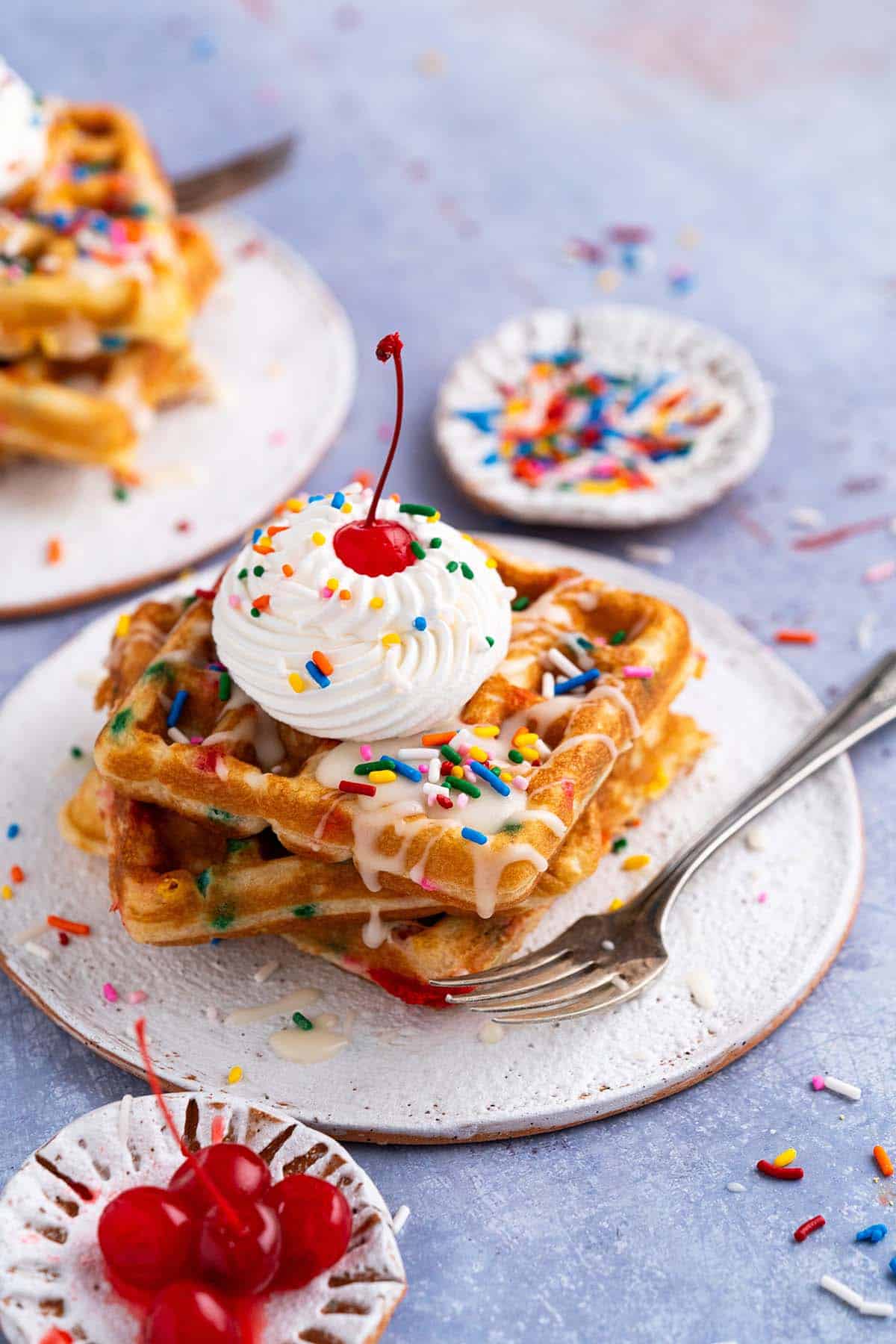 funfetti waffles topped with icing whipped cream and sprinkles