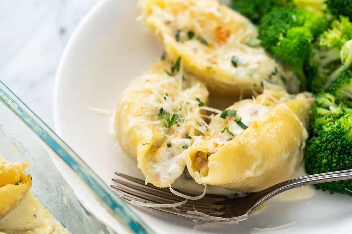 close up of chicken alfredo stuffed shells with broccoli in white bowl with fork