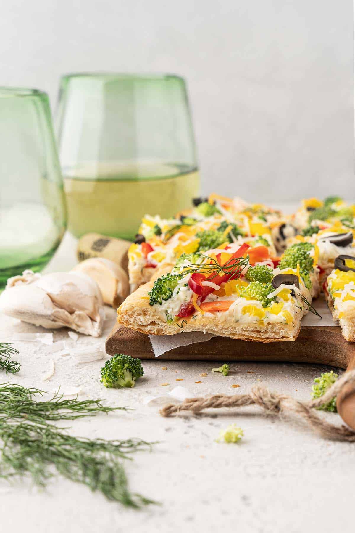 front view of cold veggie pizza squares with glasses of white wine
