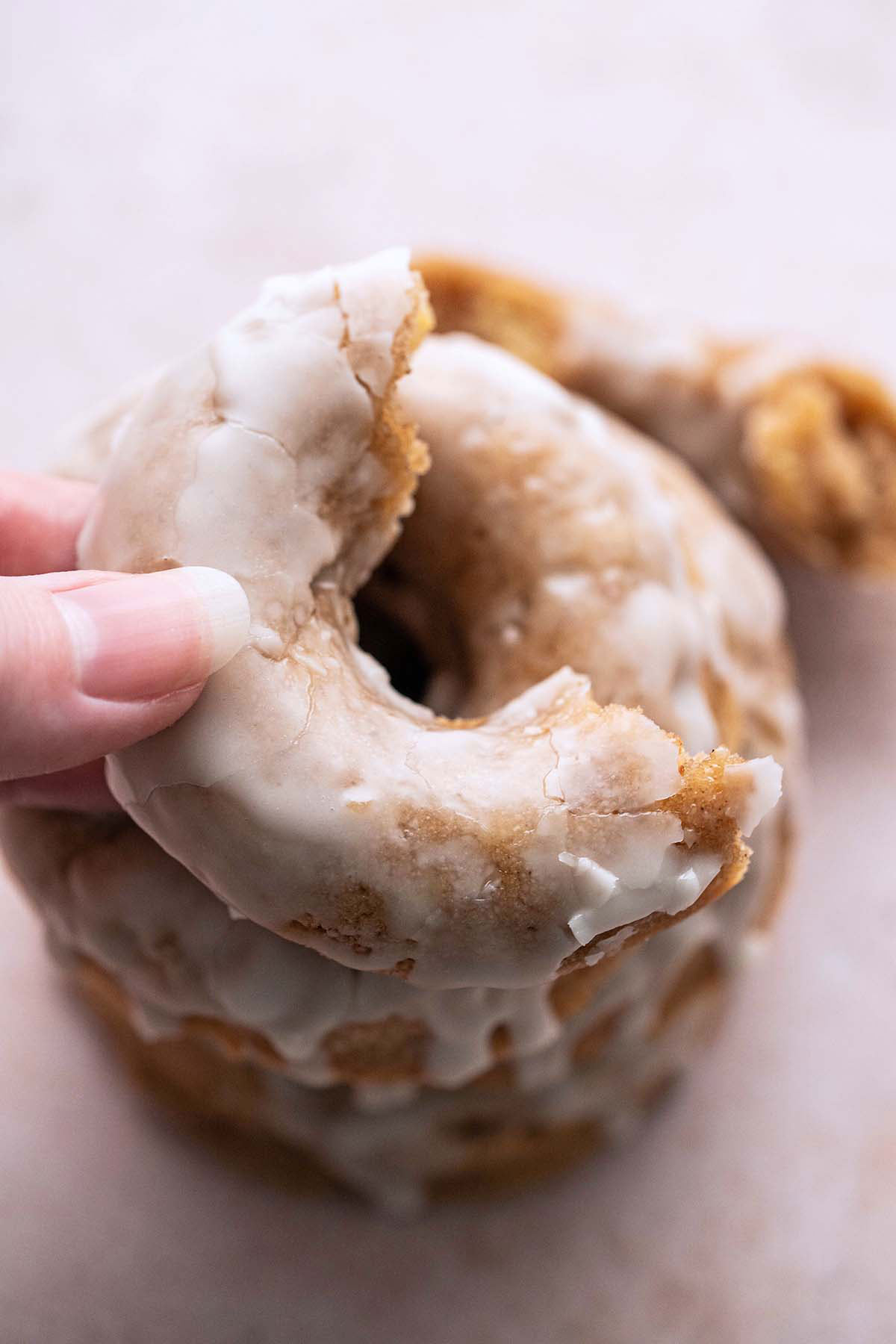 hand holding half eaten homemade apple cider doughnut over stack of doughnuts