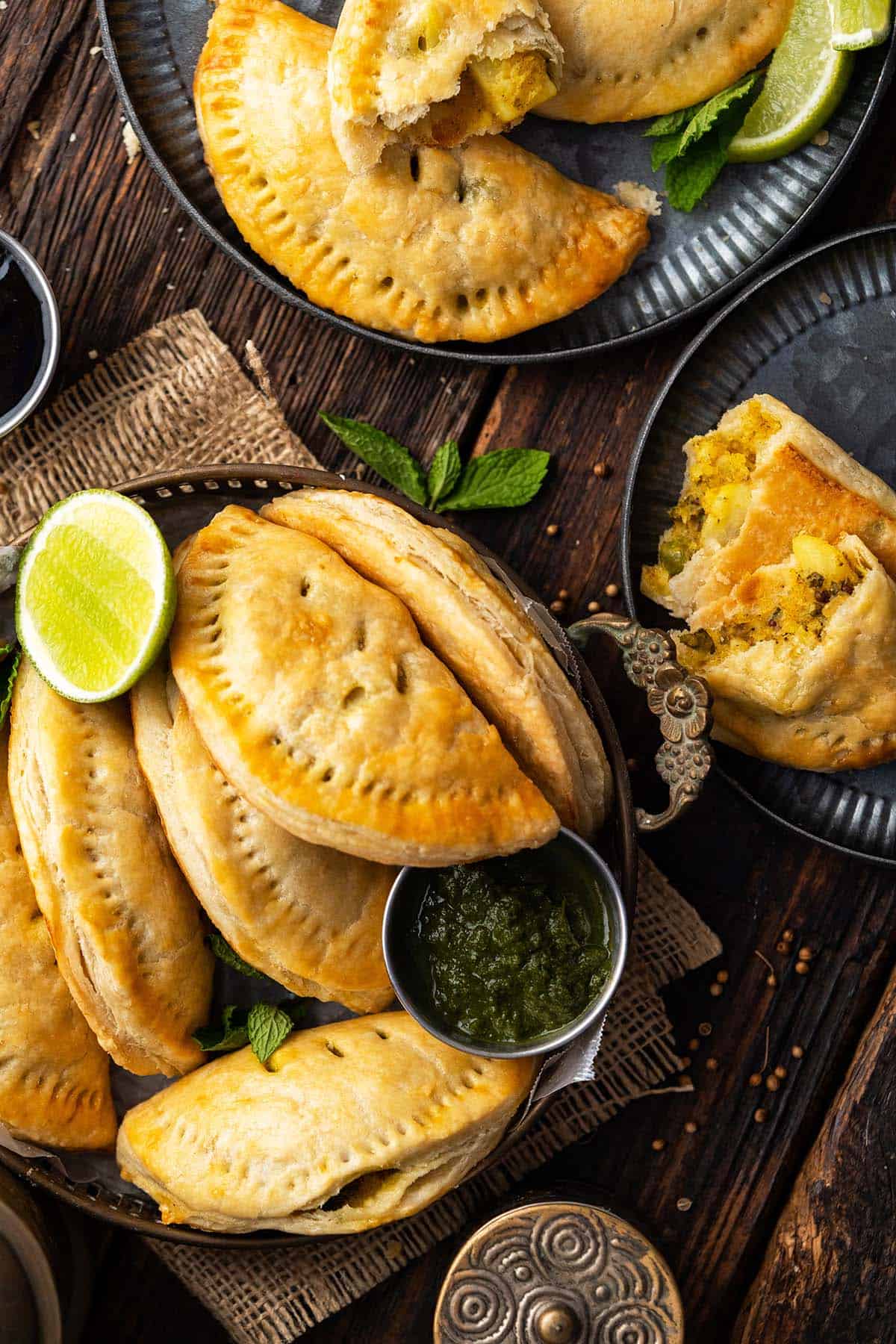 spread of vegetarian curry puffs on wooden table with mint chutney and tamarind chutney