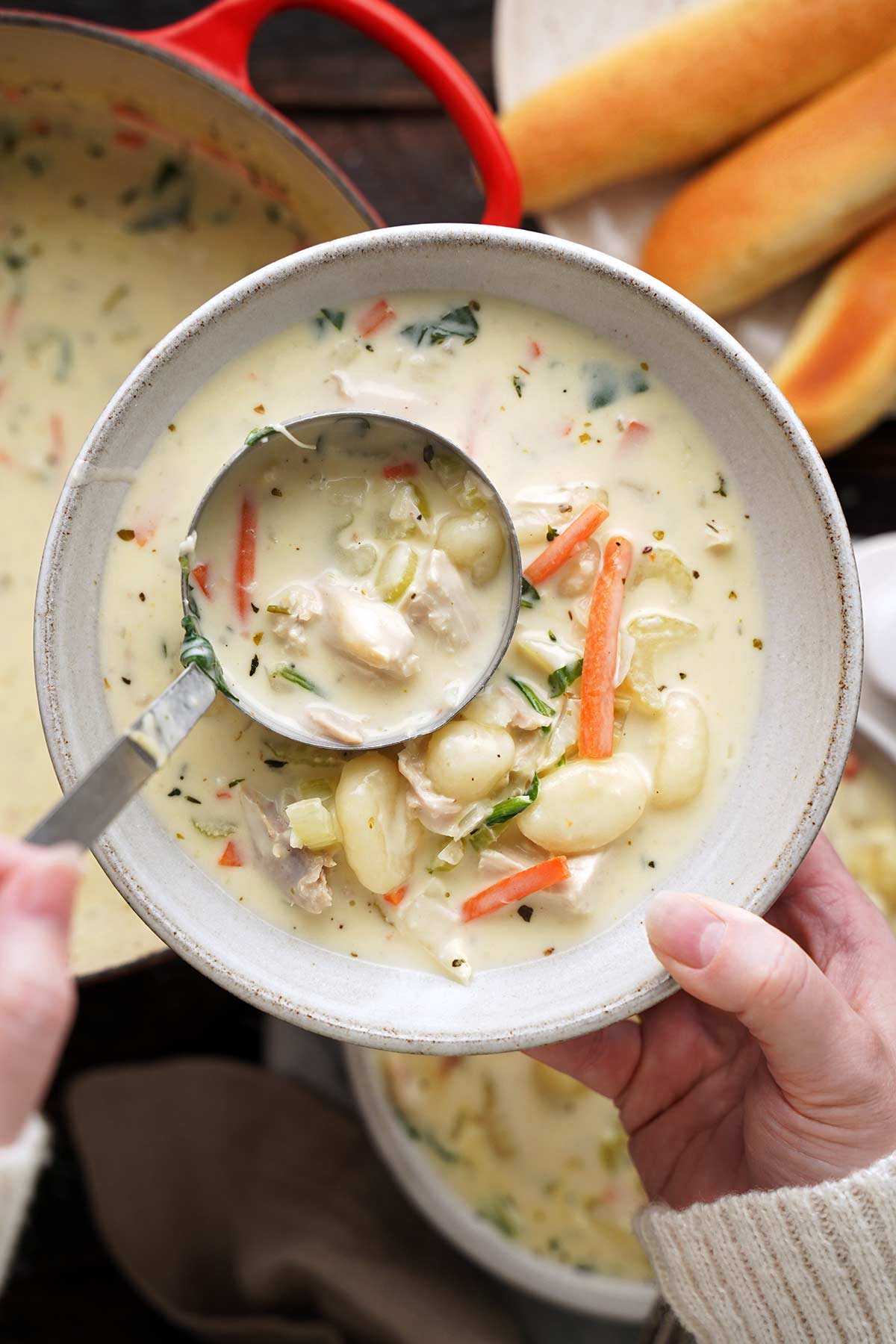hand ladling creamy chicken gnocchi soup into bowl
