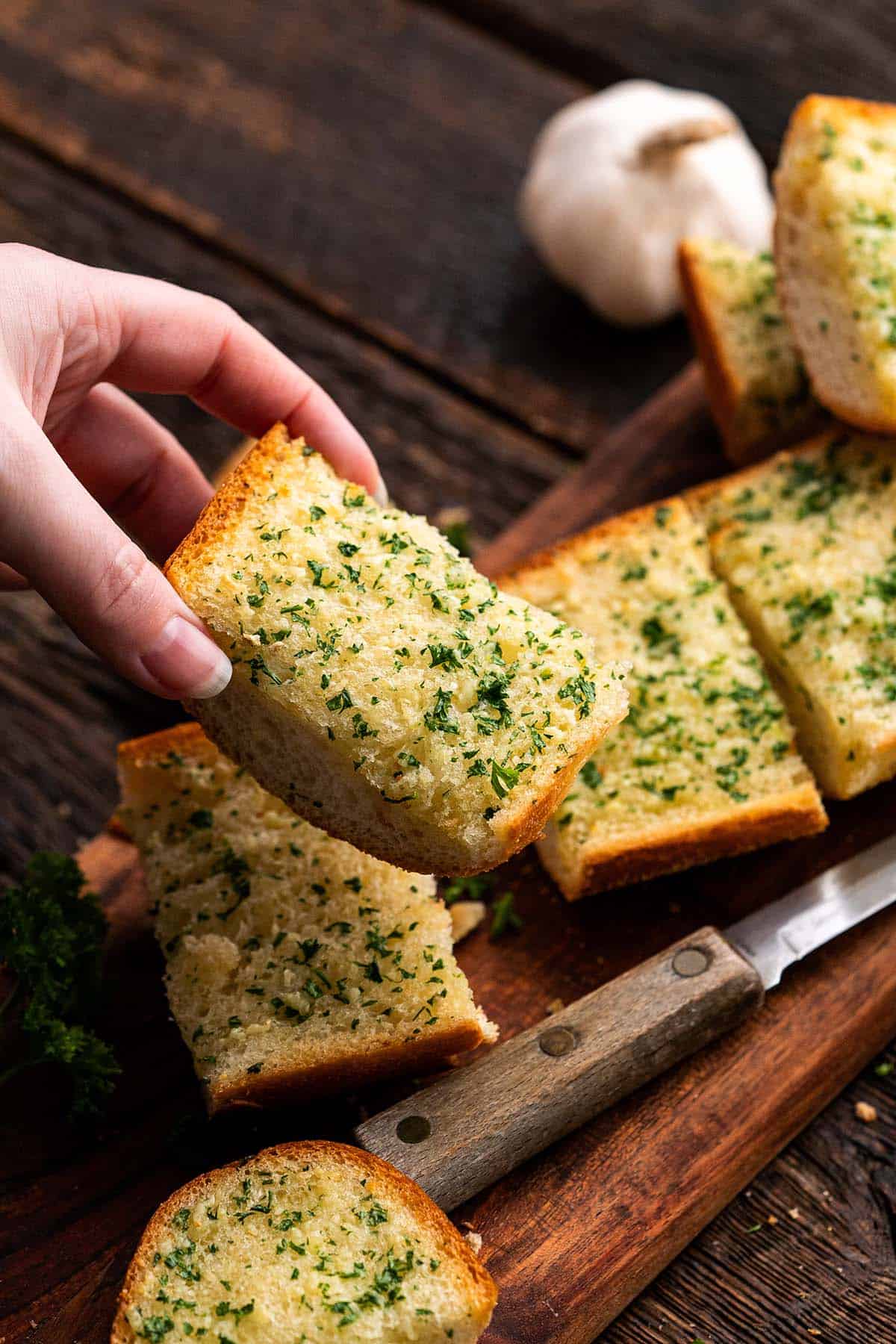 hand removing piece of parsley garlic bread from wooden tray