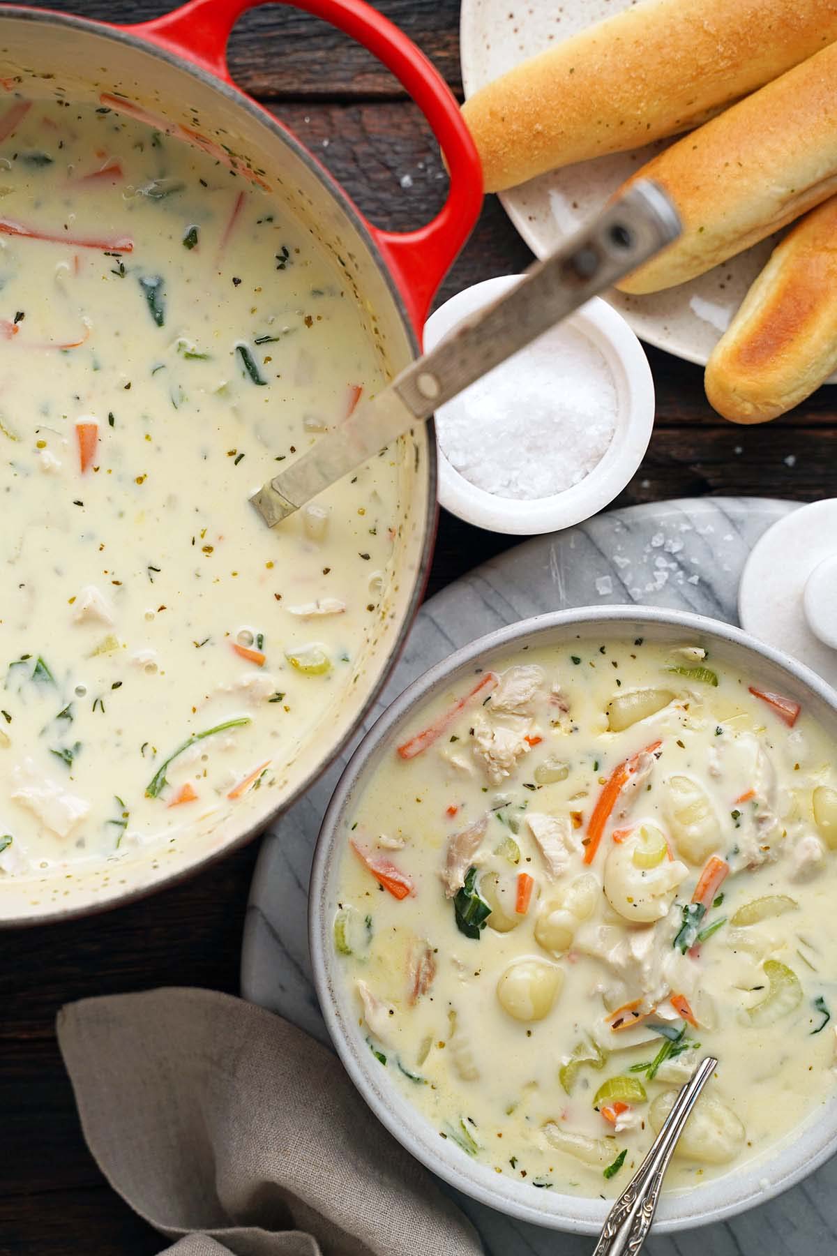 pot of homemade copycat Olive Garden chicken gnocchi soup in dutch oven with bowl and breadsticks on the side