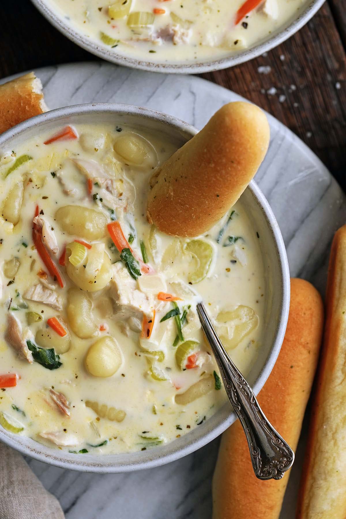 top view of creamy chicken and potato gnocchi soup with garlic breadstick in bowl