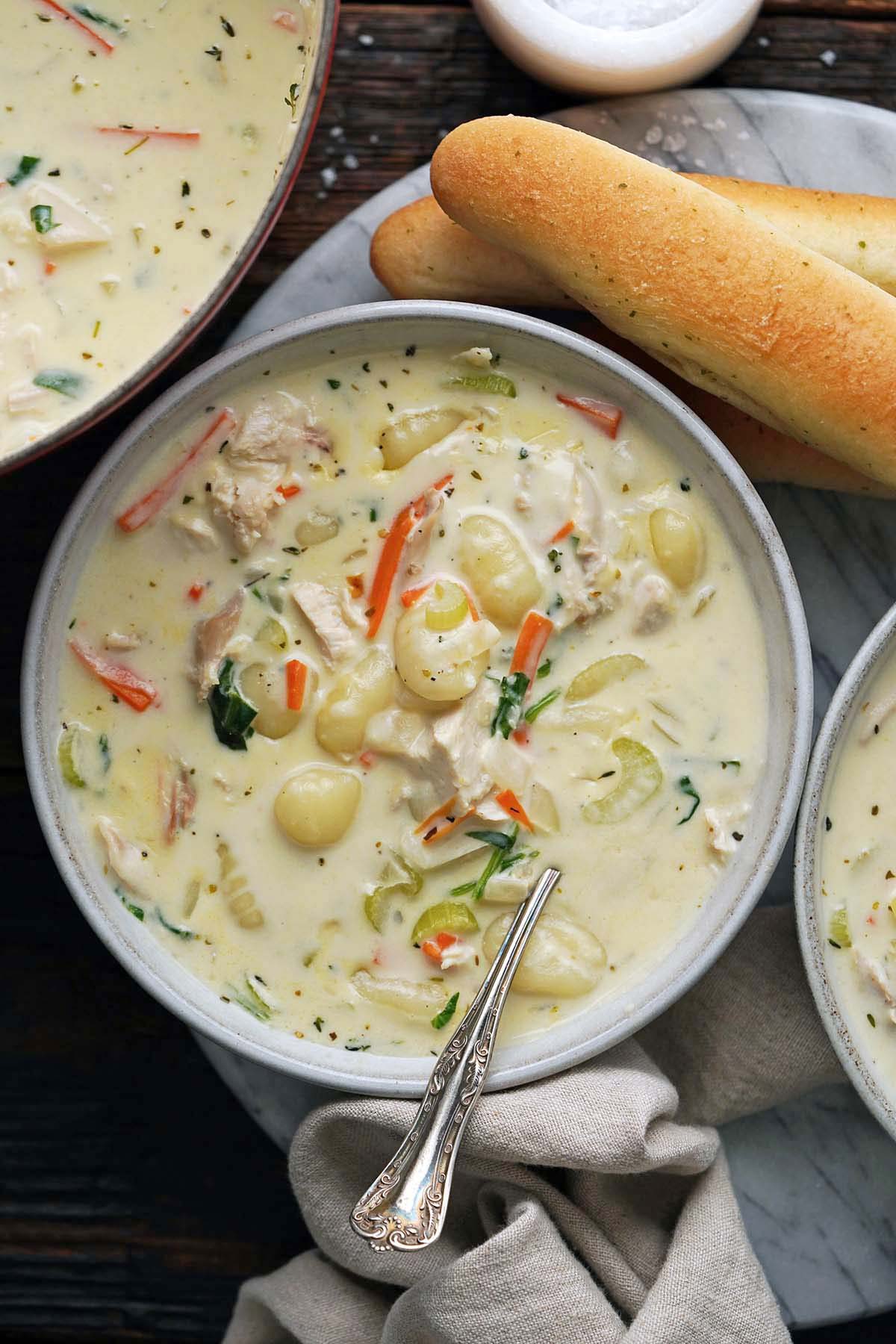 top view of Olive Garden chicken and gnocchi soup with side of breadsticks