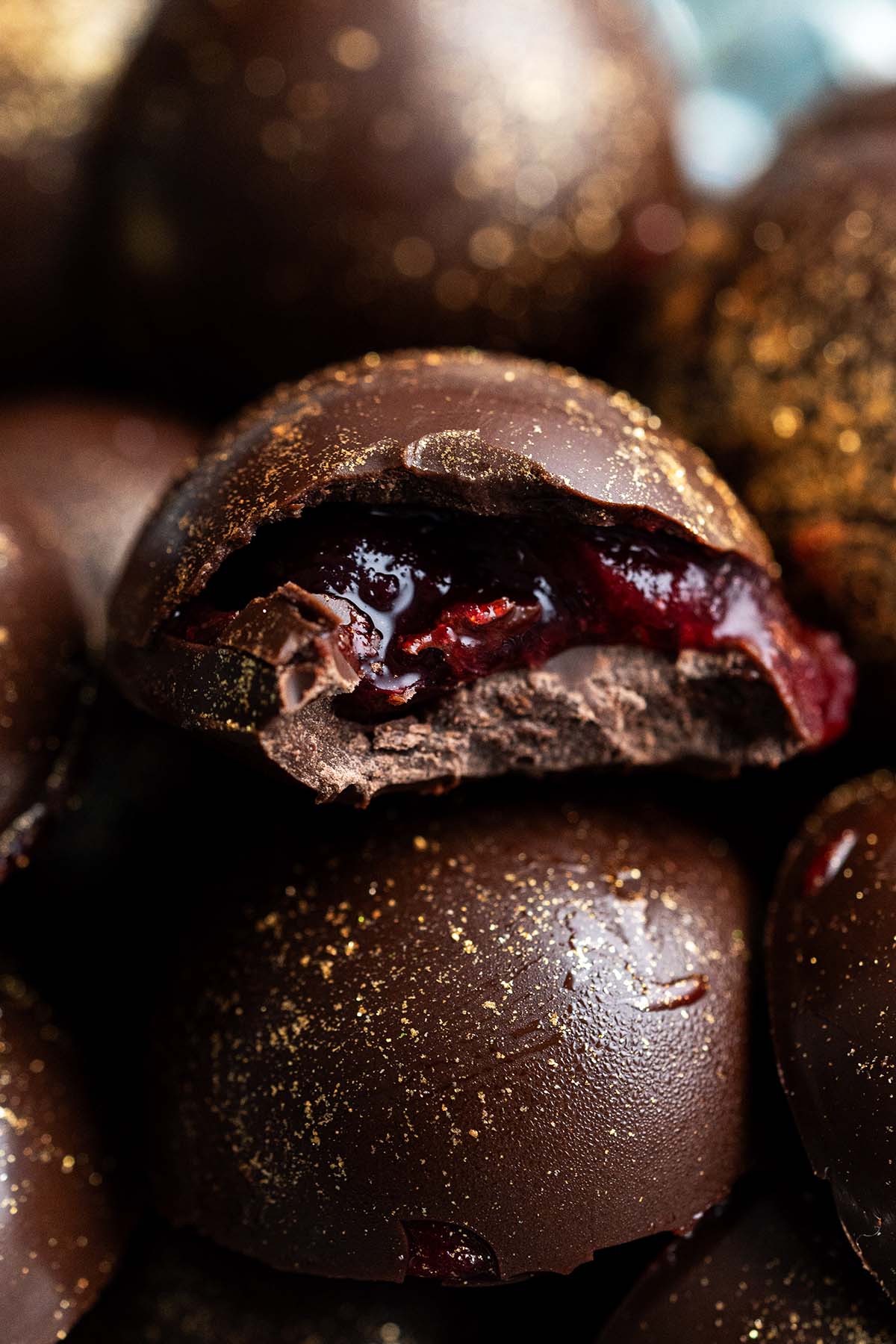 close up of cranberry chocolates with bite out of one to show cranberry cordial filling