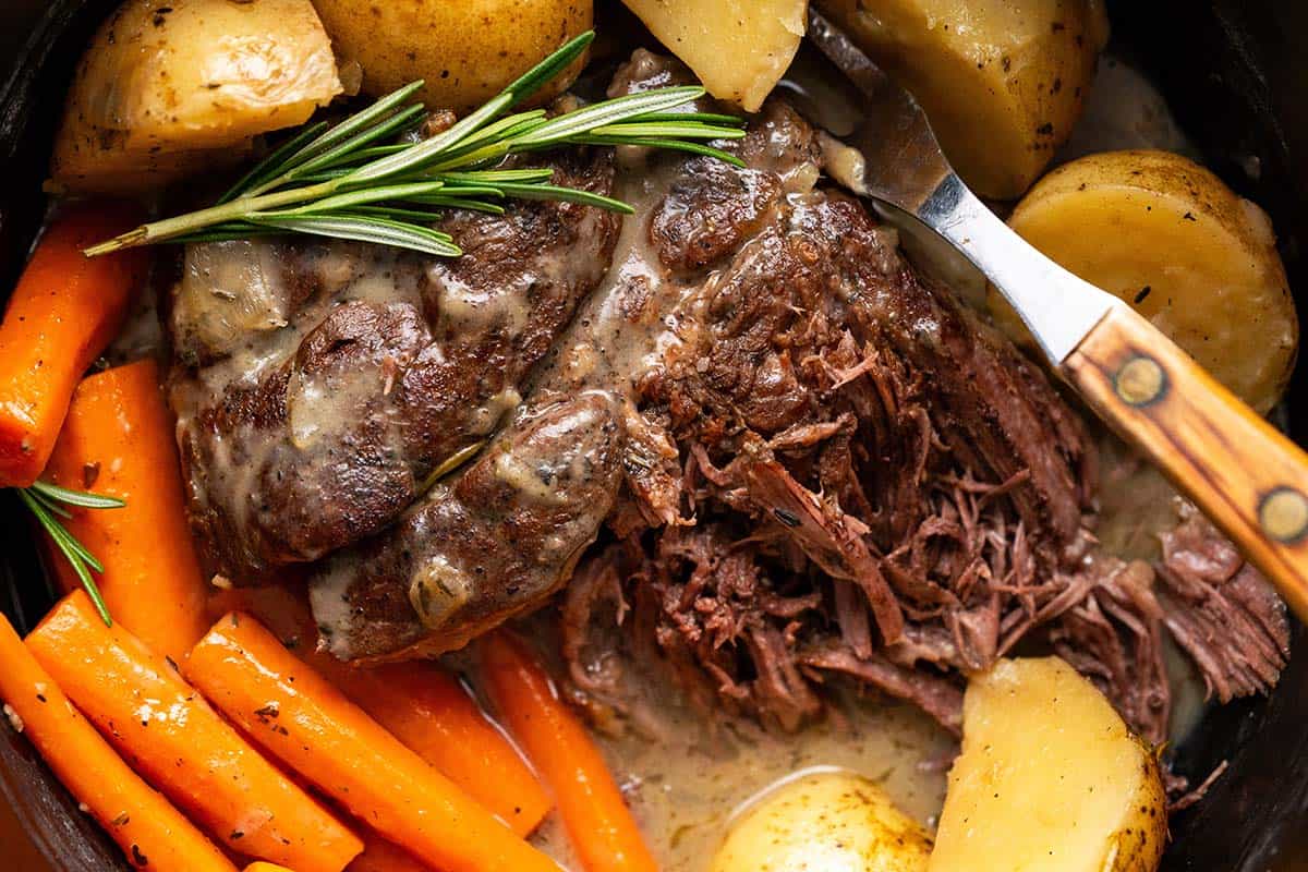 close up of fork tender beef pot roast with gravy and potatoes in dutch oven