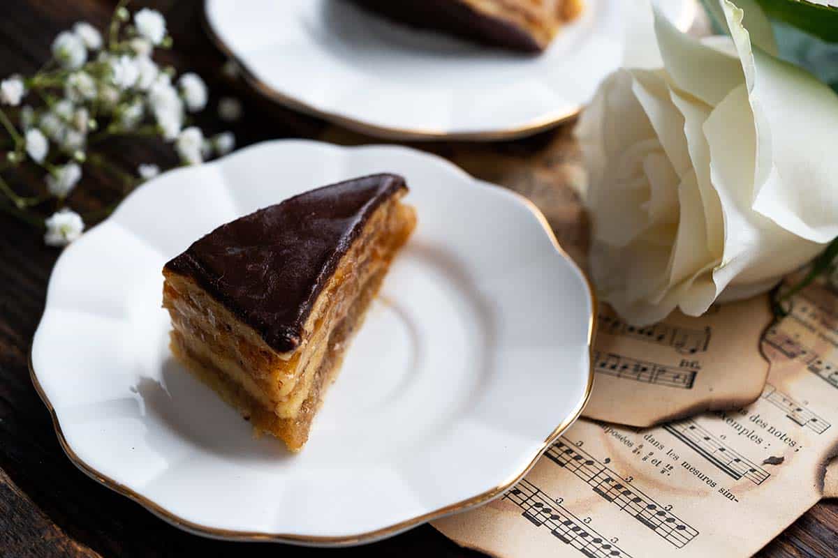 diamond shaped slice of gerbeaud cake on white dessert plate with gold trim