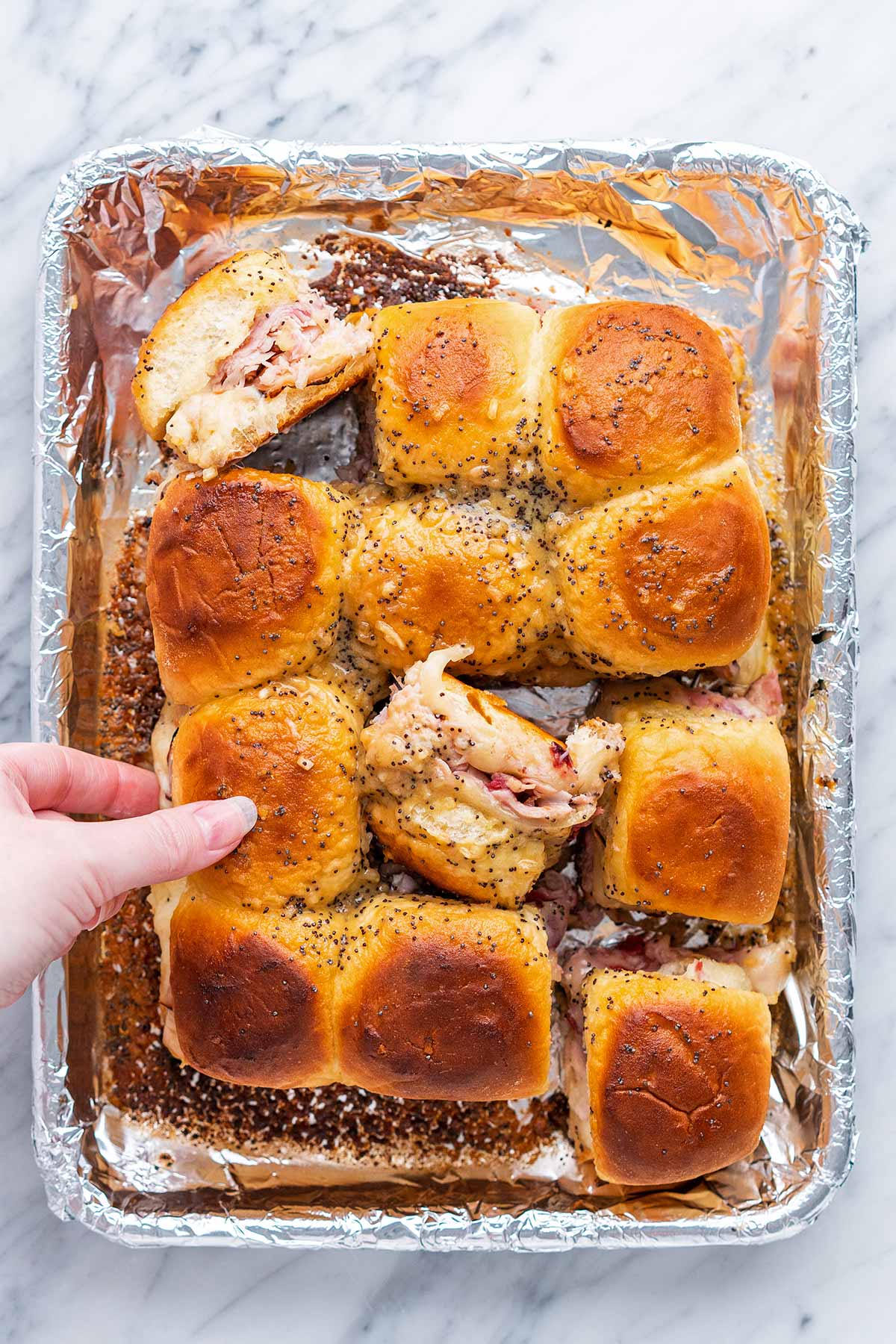 hand reaching to grab turkey Hawaiian roll slider off foil lined tray