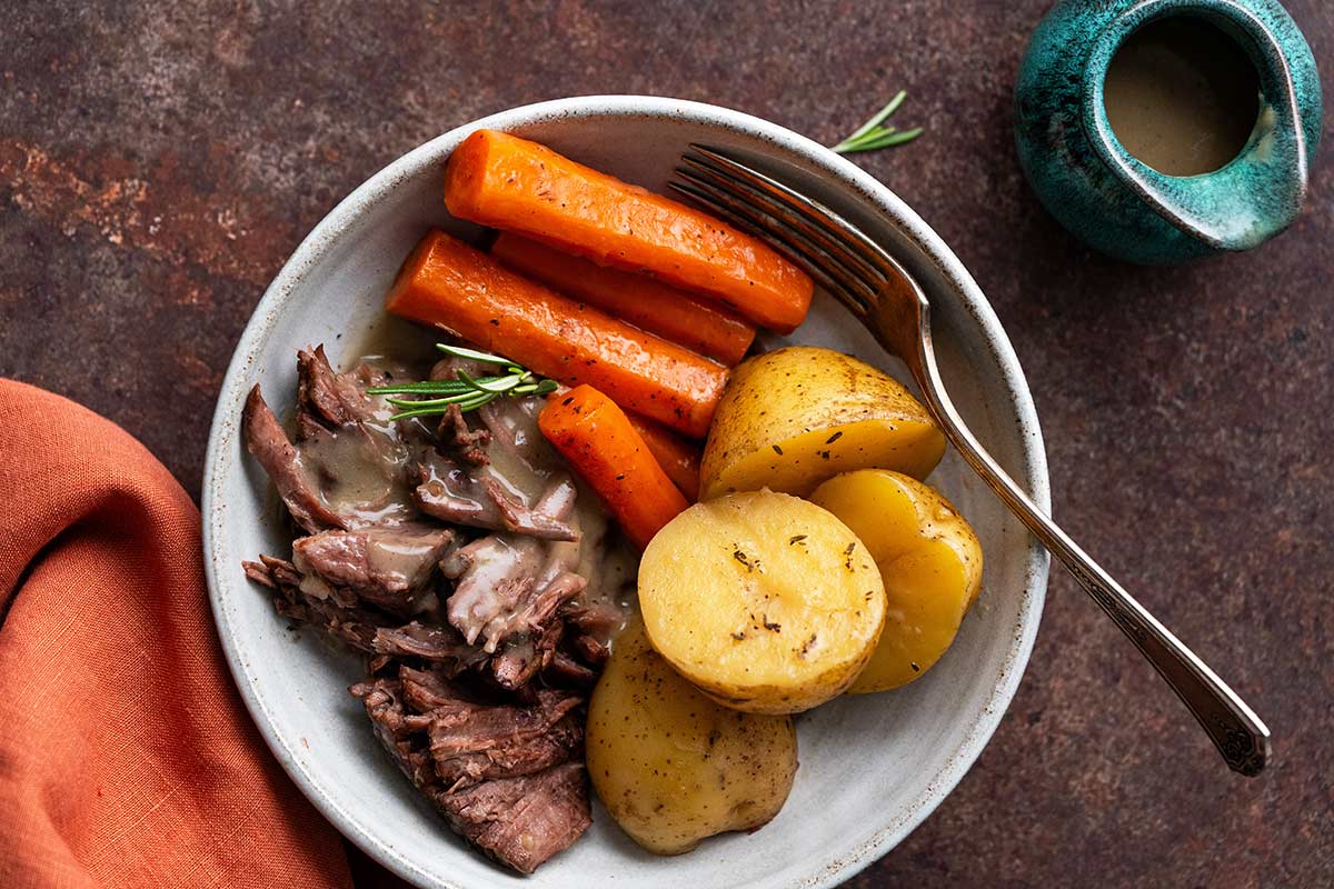 beef chuck roast dutch oven meal plated with vegetables and gravy
