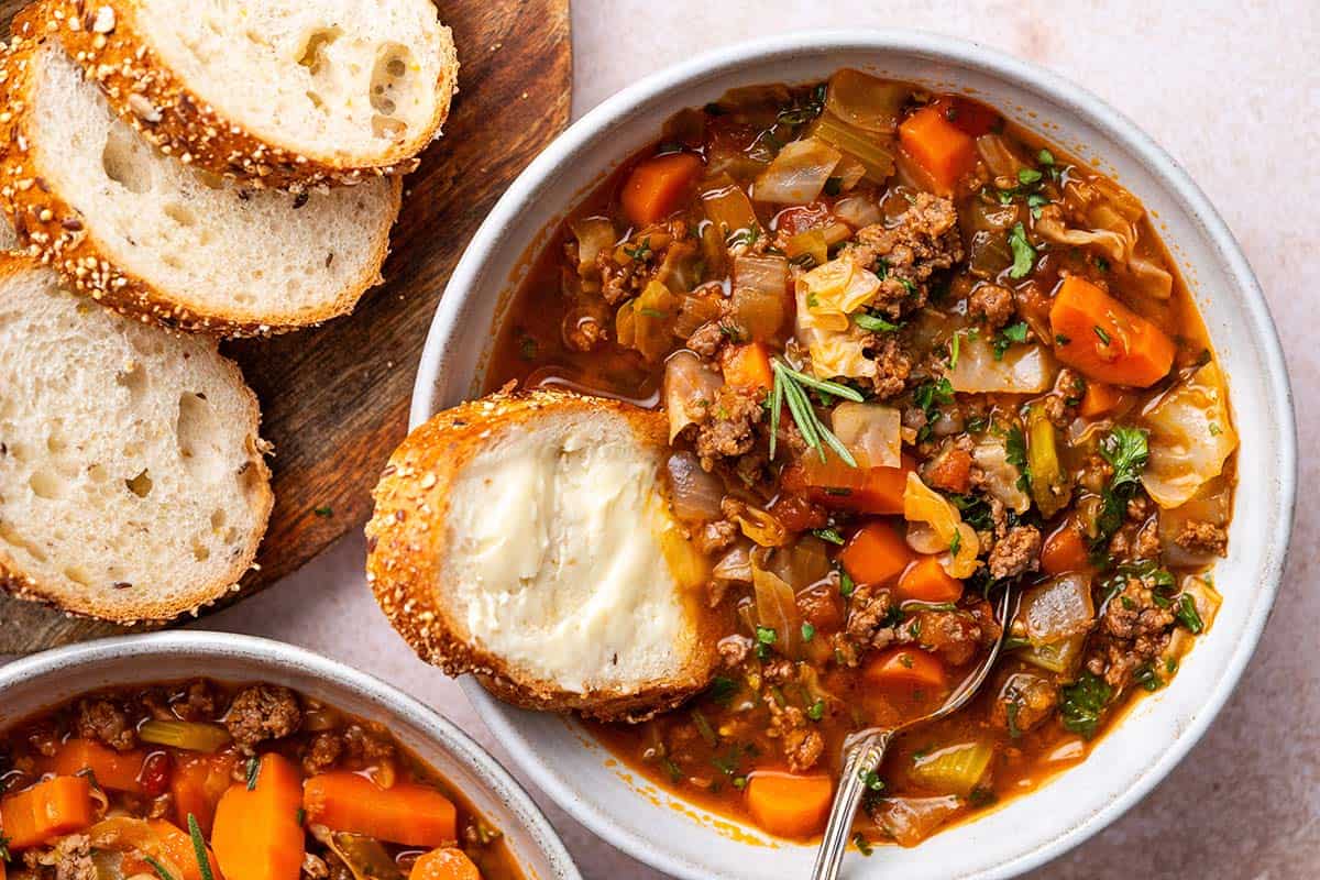 close up top view of stoneware bowl with hamburger cabbage soup with buttered bread