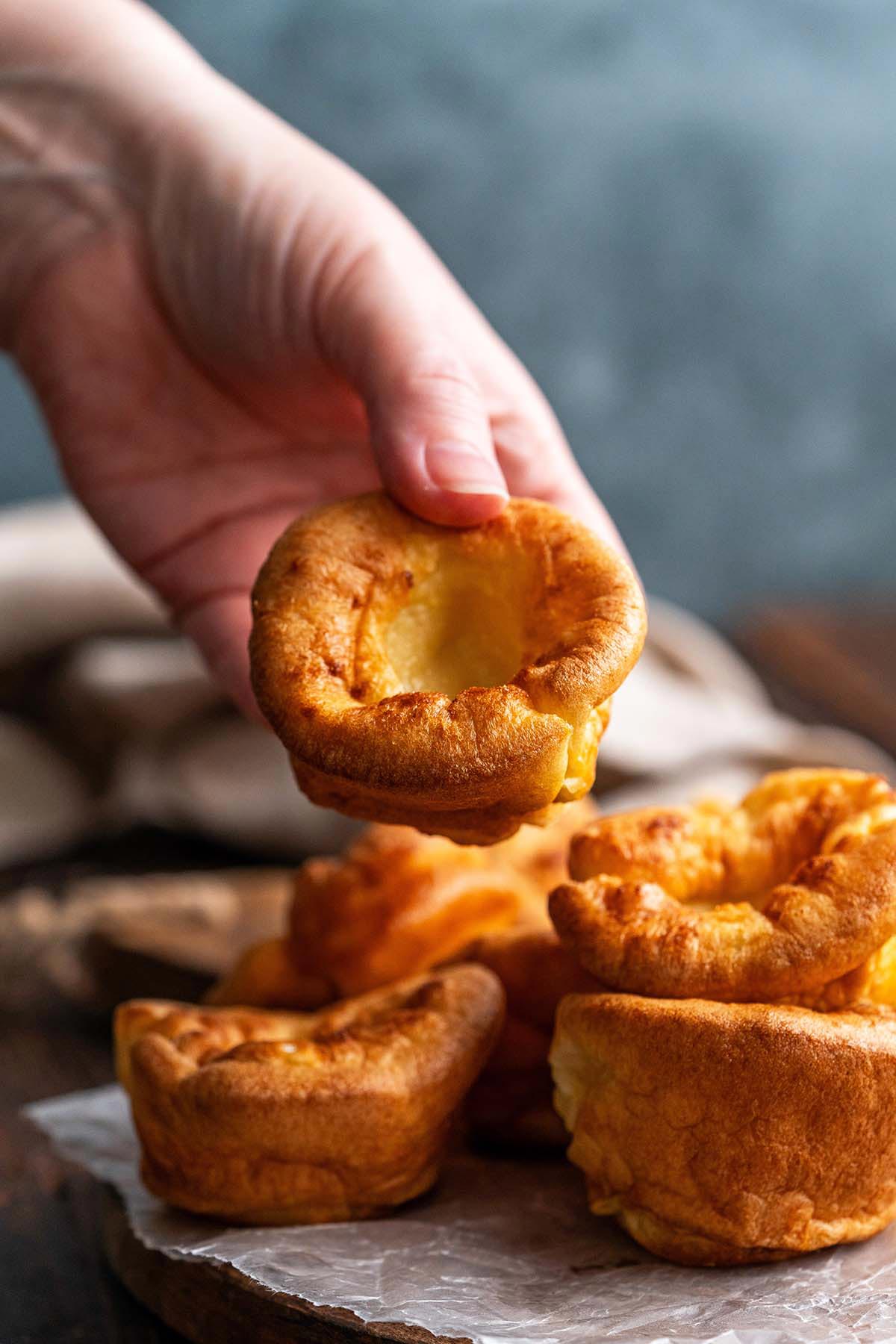 hand holding Yorkshire pudding above platter of puddings