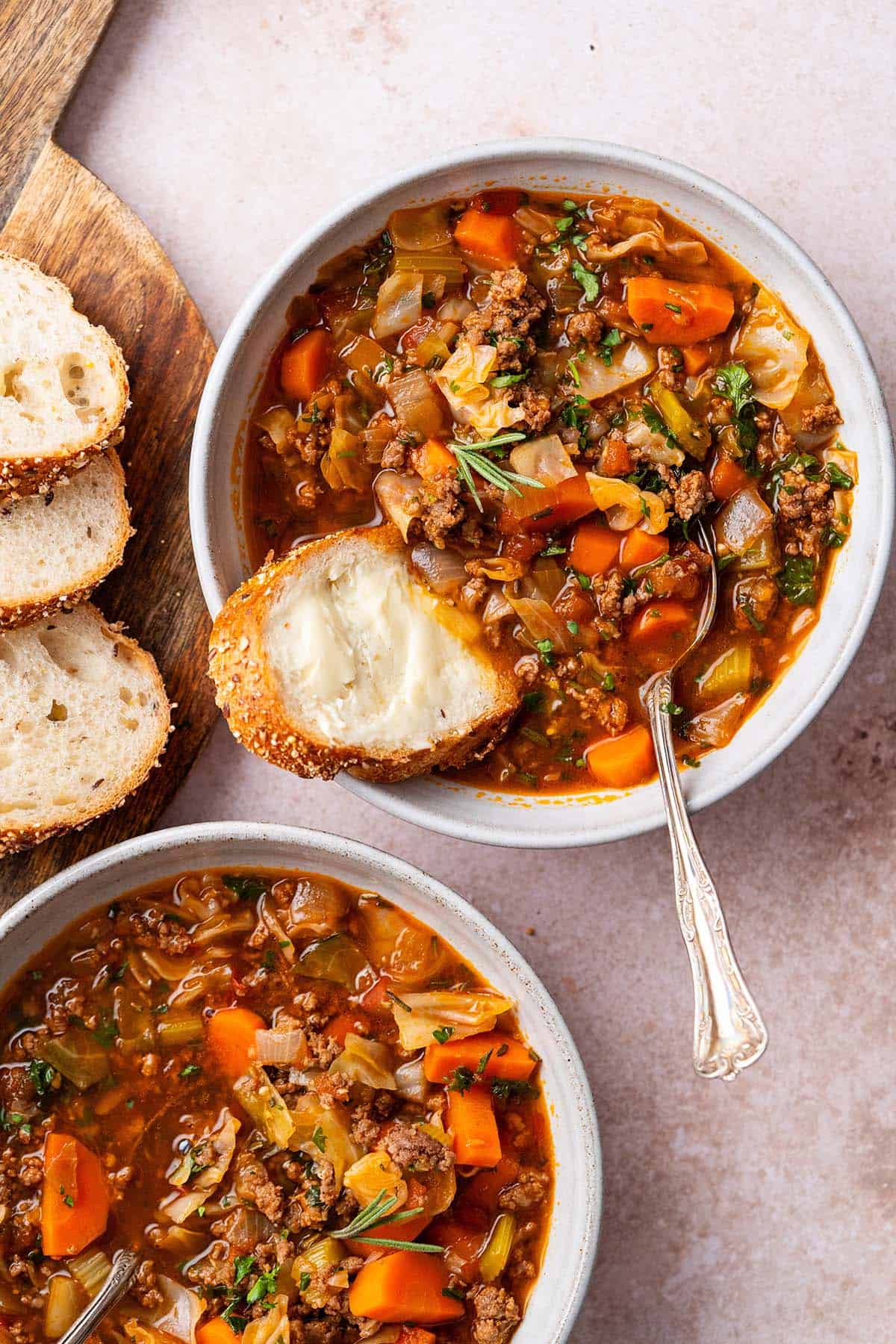 tomato cabbage soup with vegetables and hamburger in bowls with sliced bread