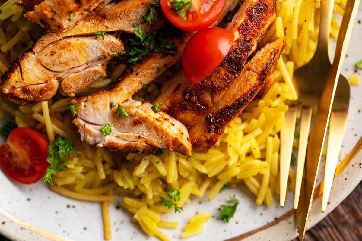 close up of chicken with blackening seasoning and yellow rice on plate