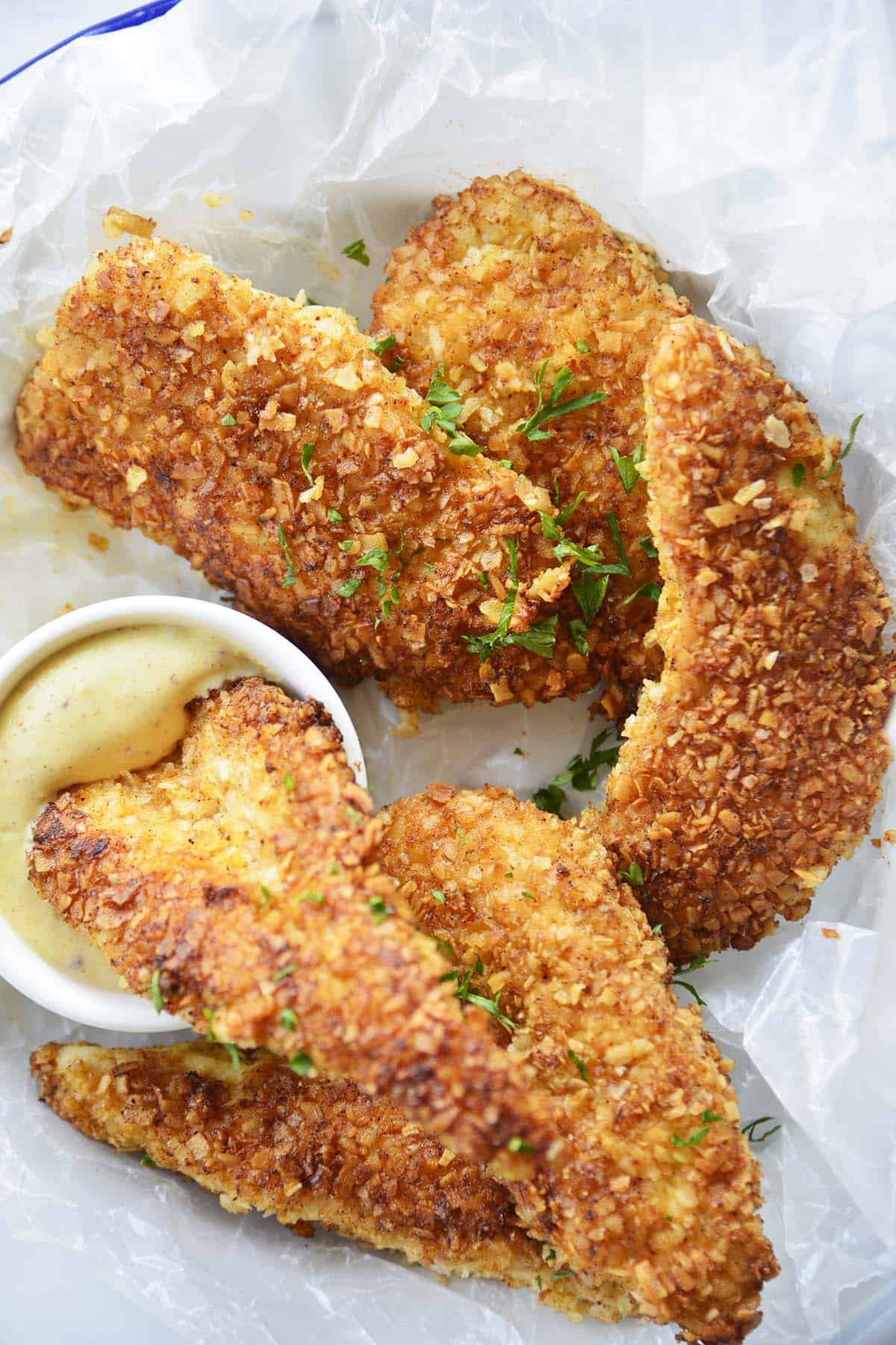 close up top view of crispy coconut chicken finger dipping in creamy dressing