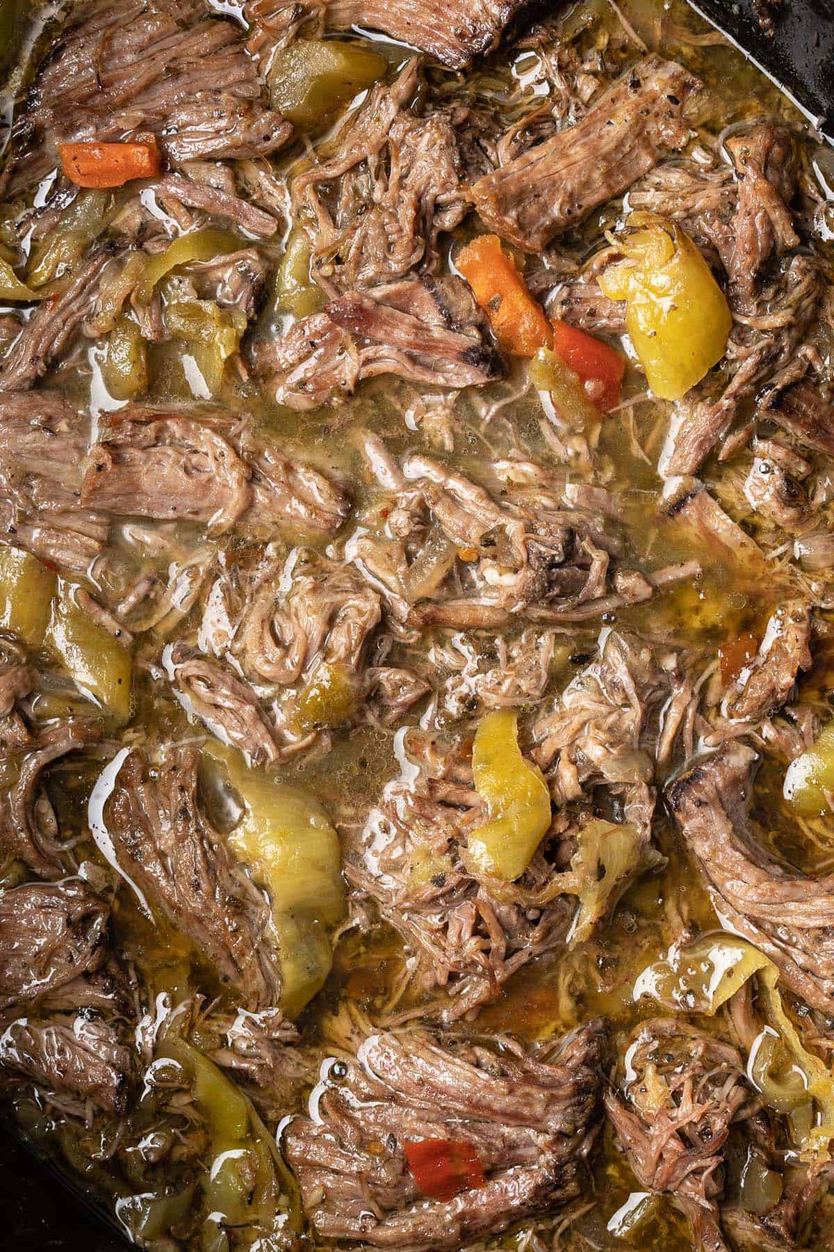 close up top view of shredded italian beef with pepeprs in crockpot