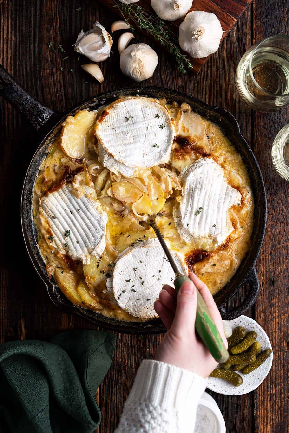 hand scooping tartiflette out of cast iron skillet