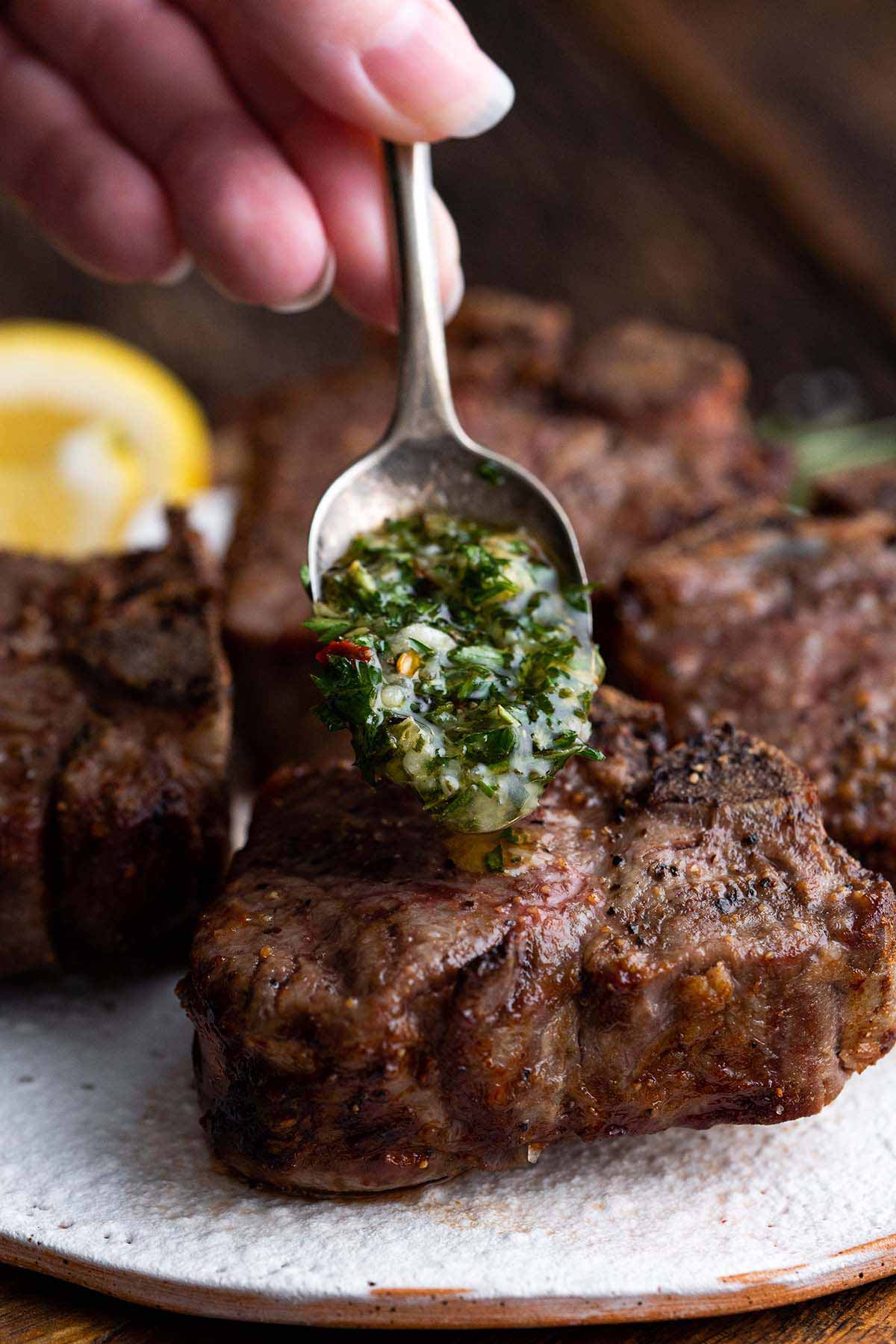 hand spooning fresh garlic herb sauce eon top of cooked lamb chops