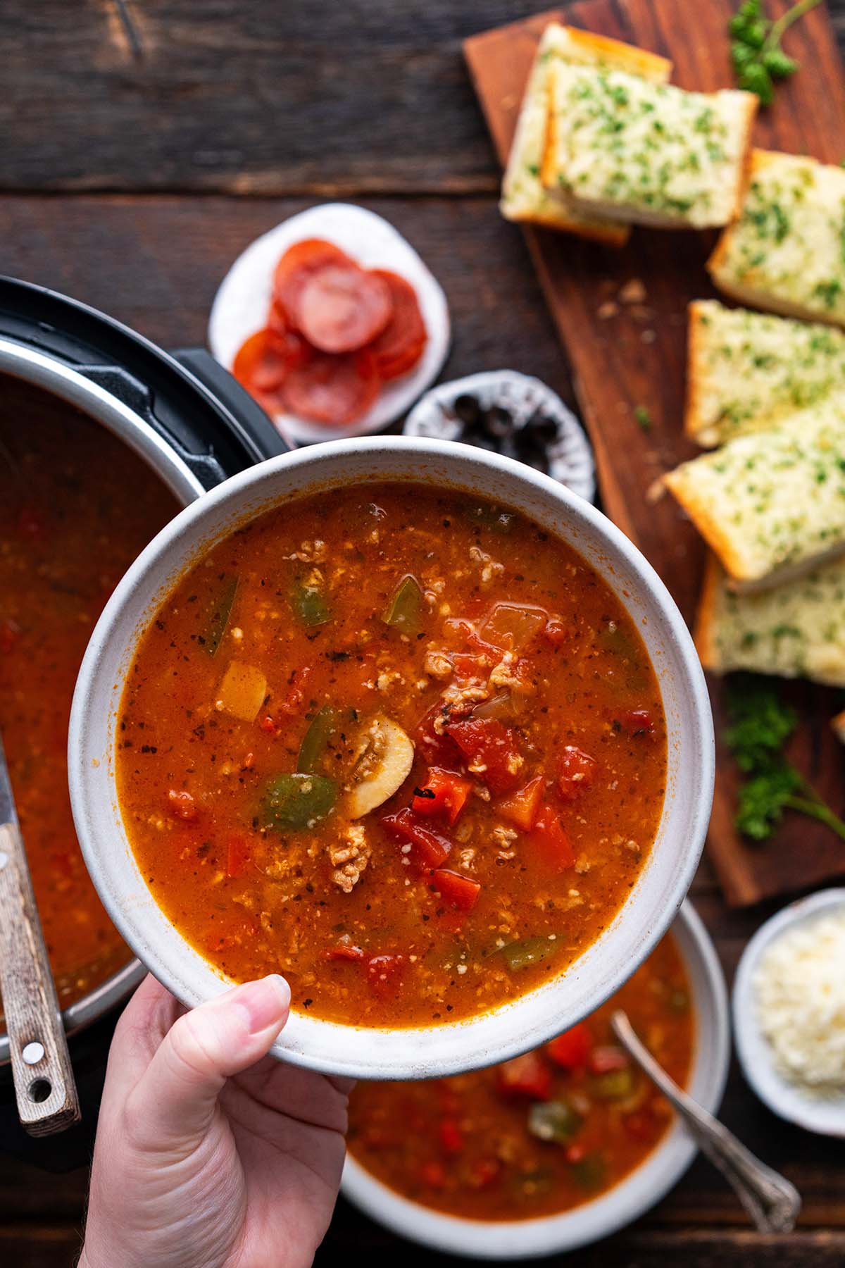 hand holding white bowl with pizza soup over instant pot