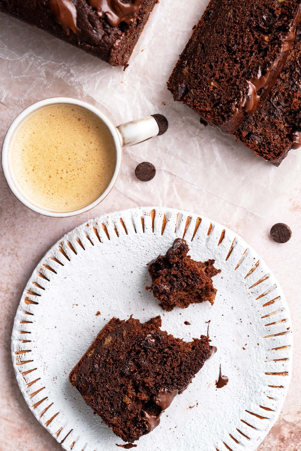 slice of partially eaten chocolate banana bread on plate with coffee