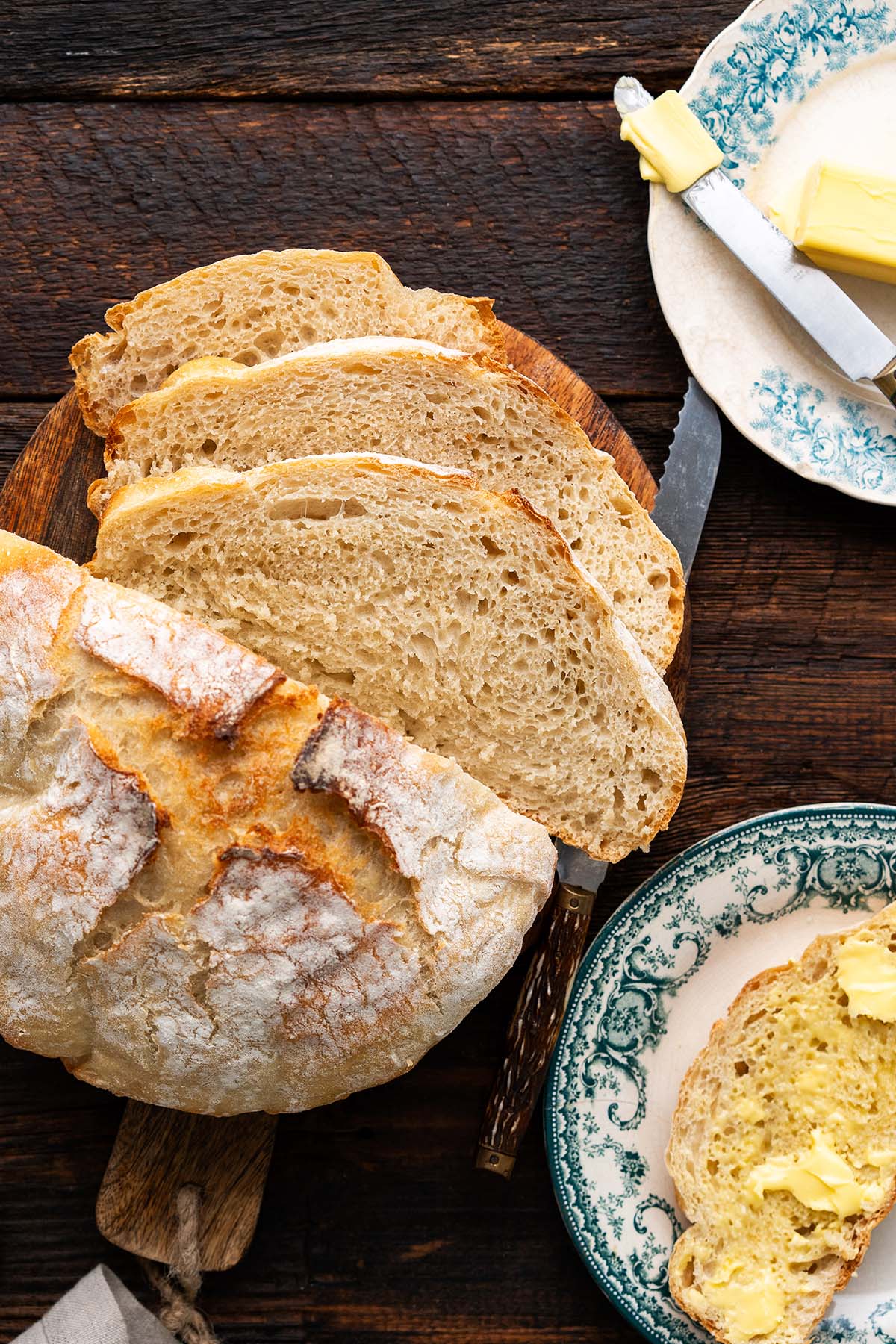 top view of loaf of homemade artisan bread recipe with buttered slice of bread on plate