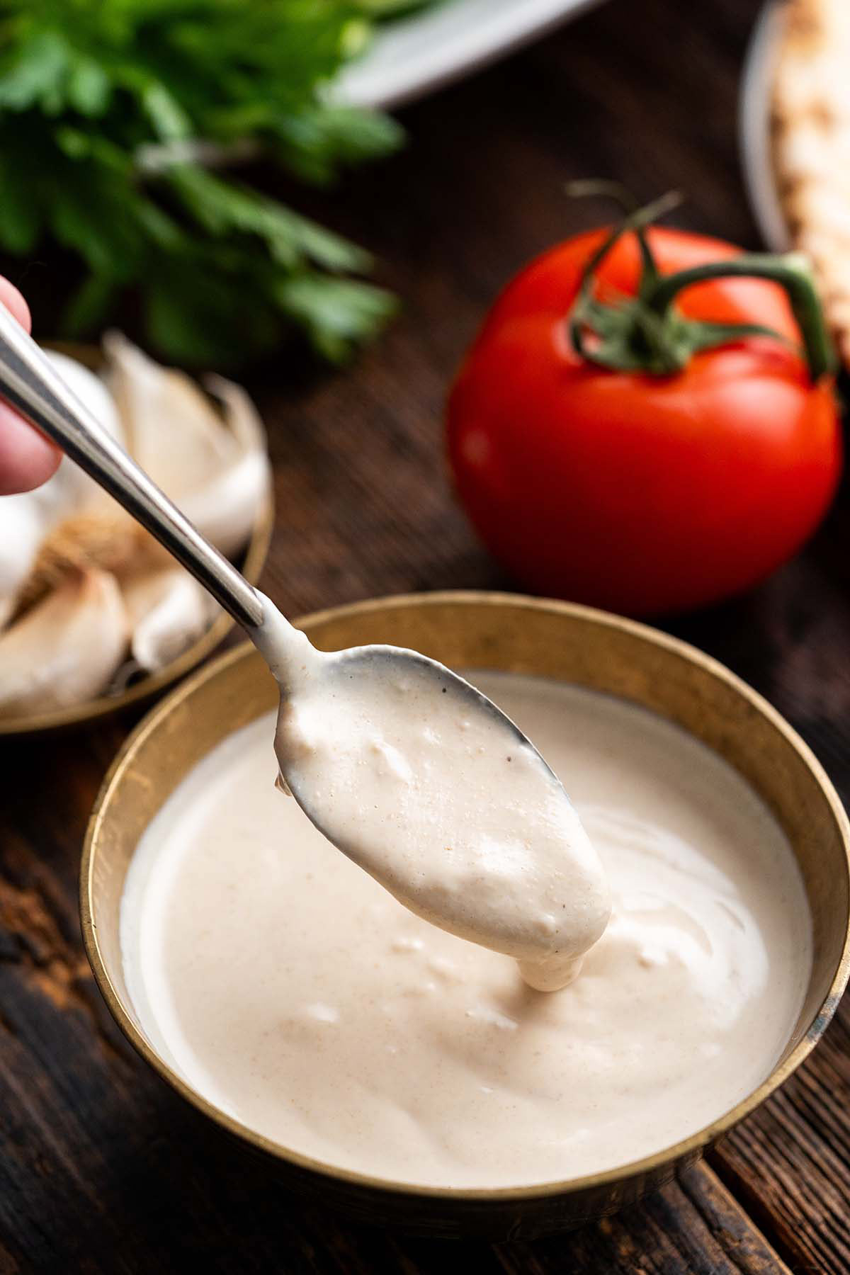drizzling yogurt shawarma sauce off spoon into bowl