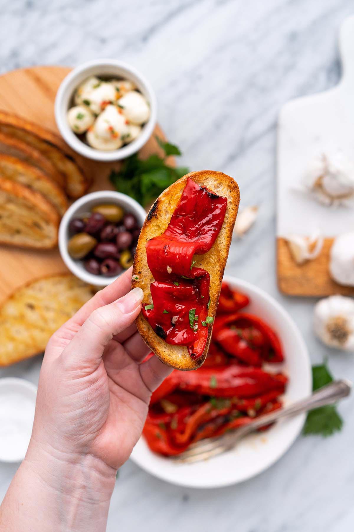 hand holding slice of toasted garlic bread topped with grilled red pepper
