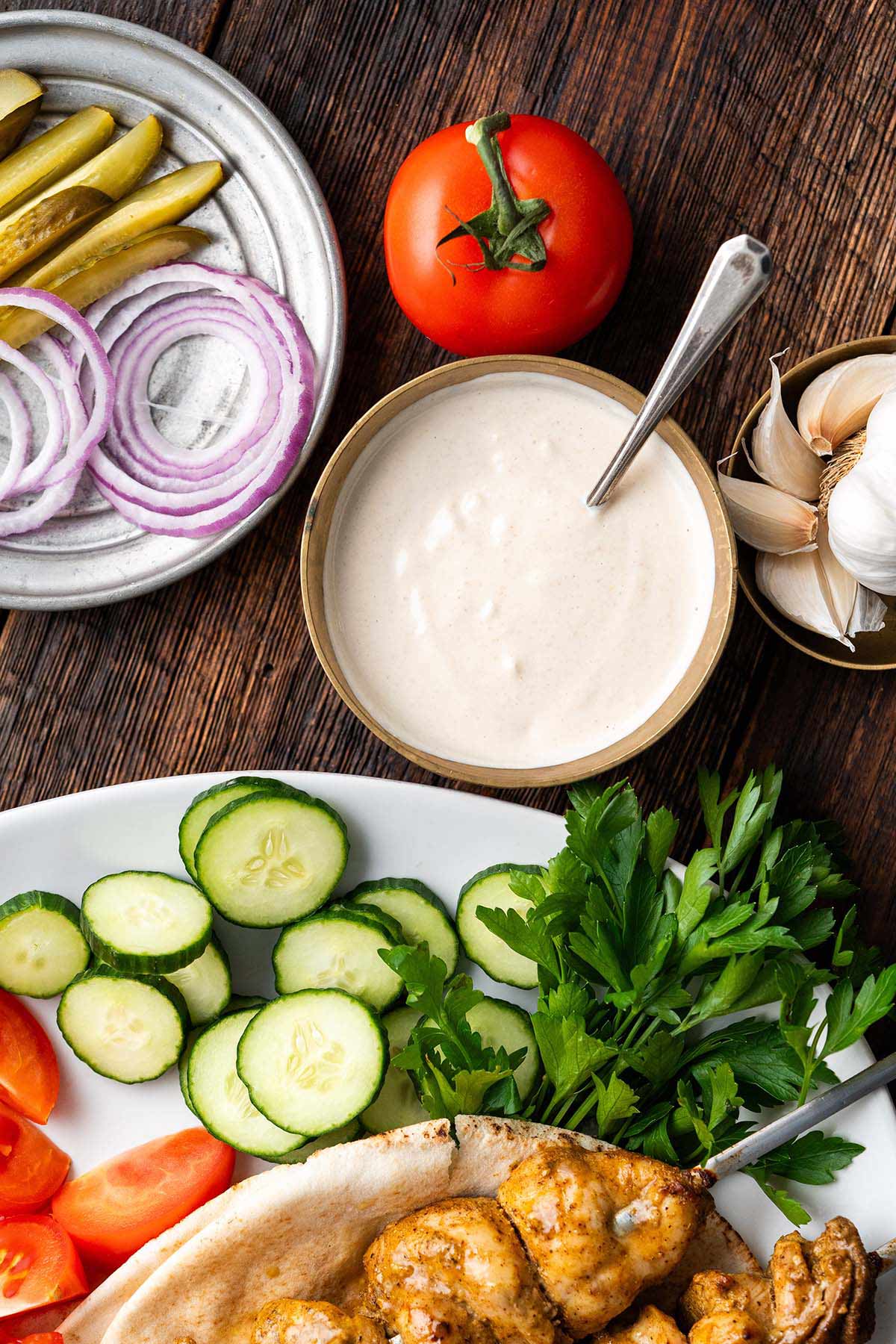 overhead view of chicken shawarma skewers with vegetables and bowl of garlic yogurt tahini sauce