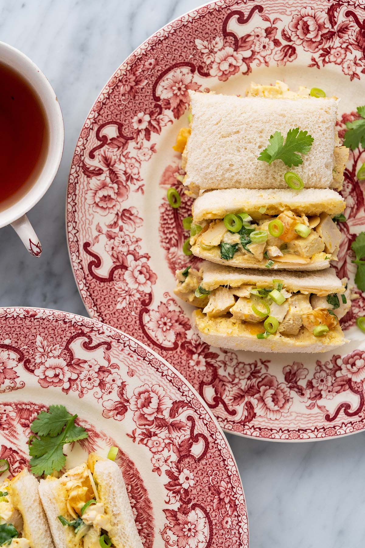 top view of chicken salad finger sandwiches on english china plates with tea cup