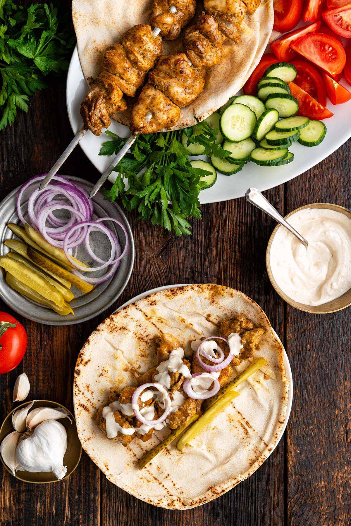 top view of spread of chicken thigh shawarma skewers with sauce and pita bread for sandwiches