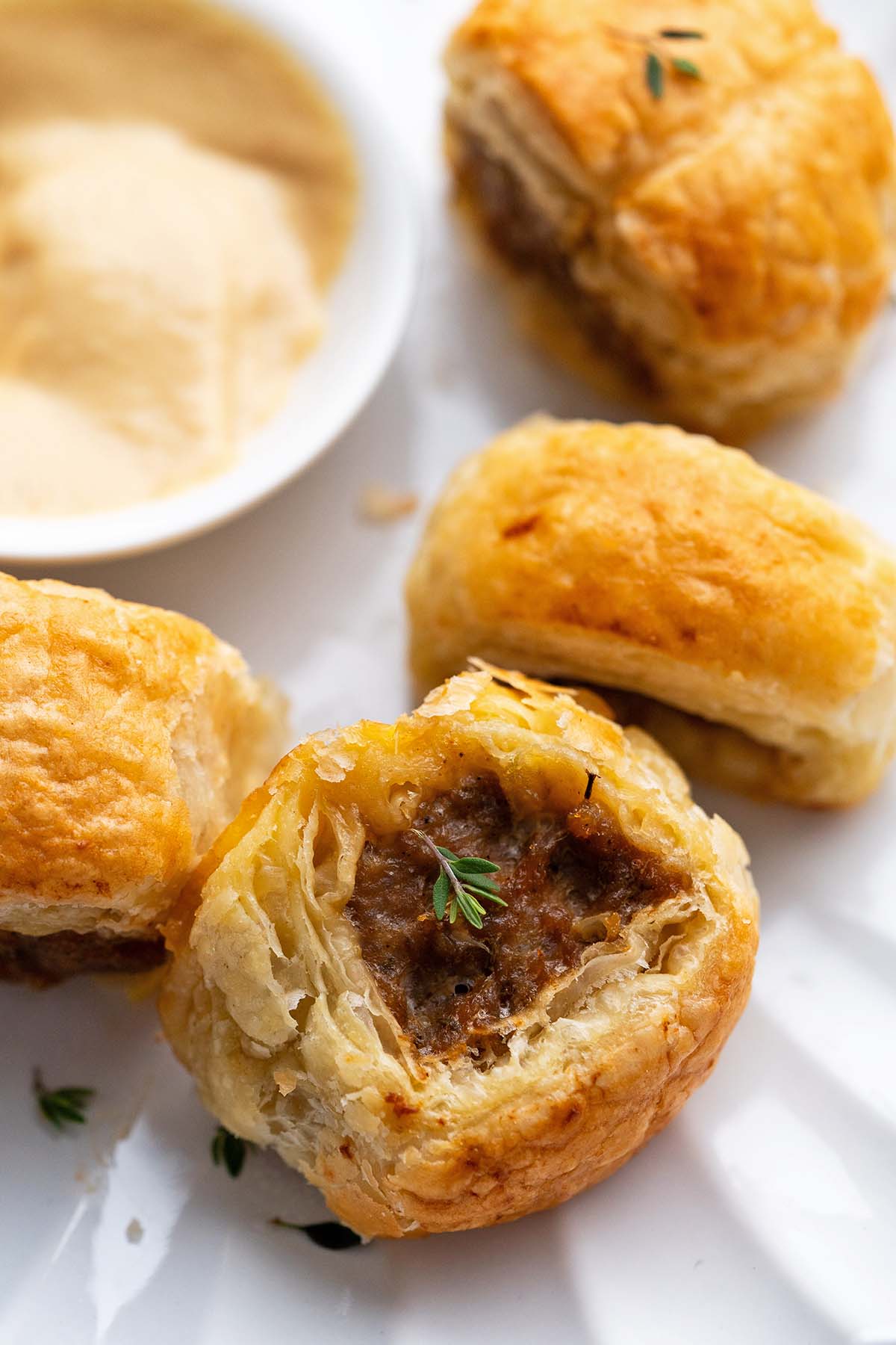 close up of crispy mini sausage roll on white plate with small dish of dijon in background