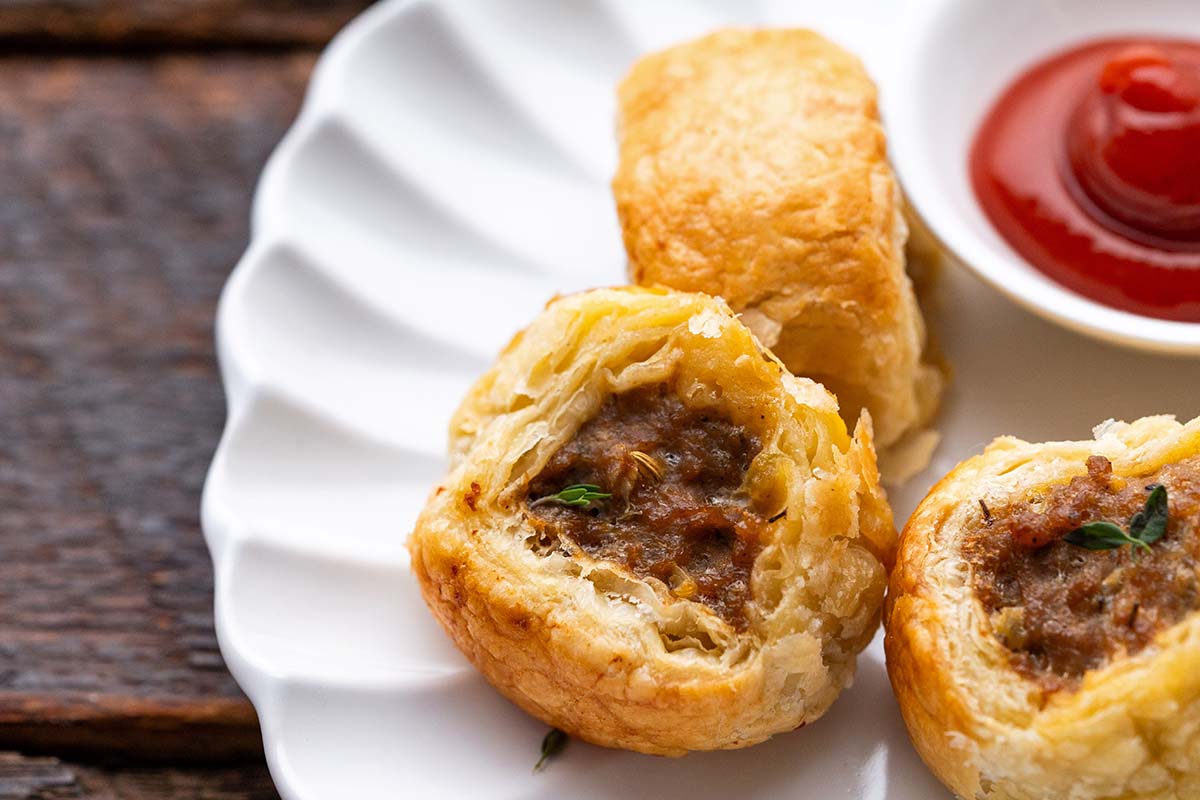 close up of flaky puff pastry sausage rolls with side of ketchup