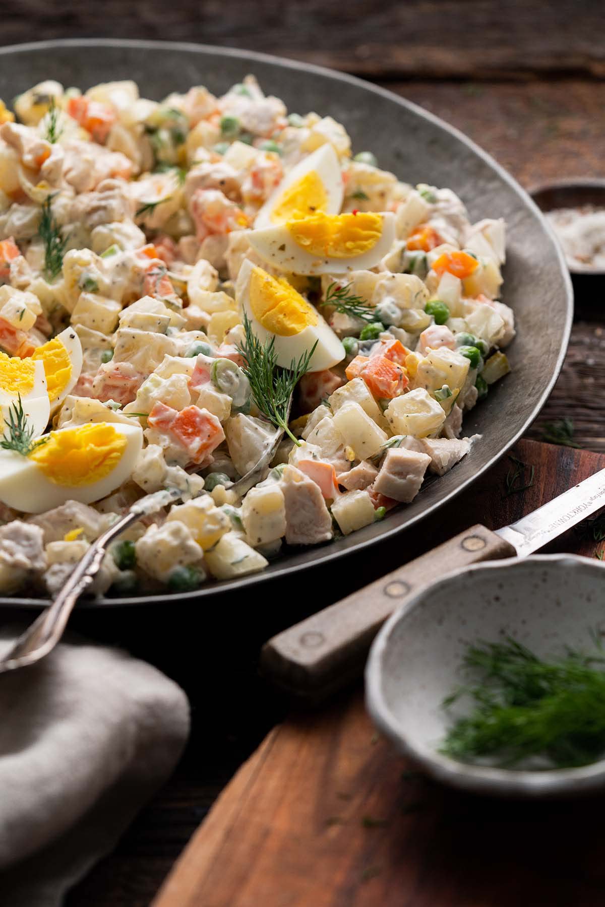 front view of serving bowl with olivier salat topped with hard boiled egg and dill