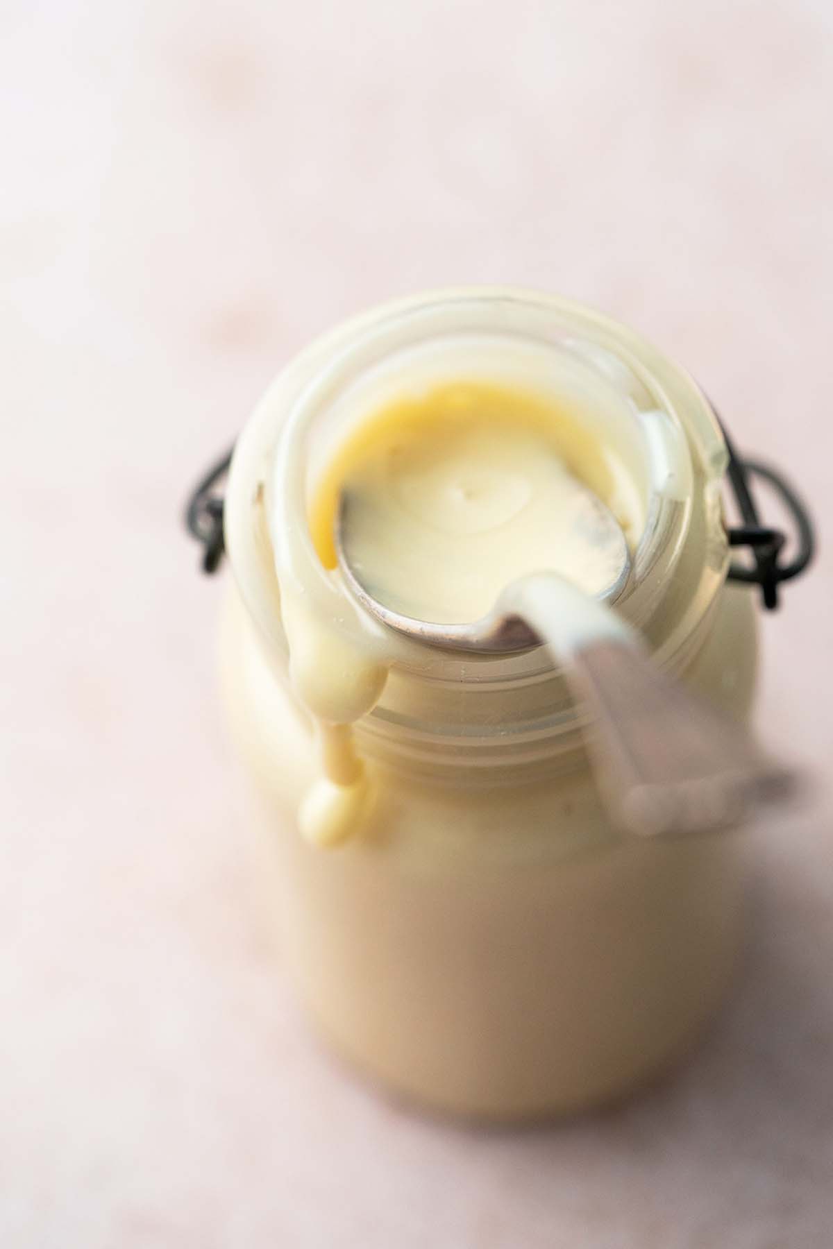 glass jar with condensed milk with vintage spoon and drip down side of jar