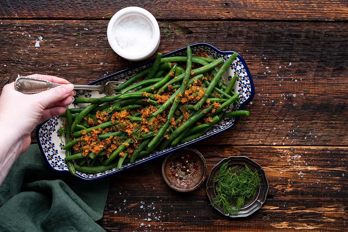 hand serving polish green beans off of tray on wooden table