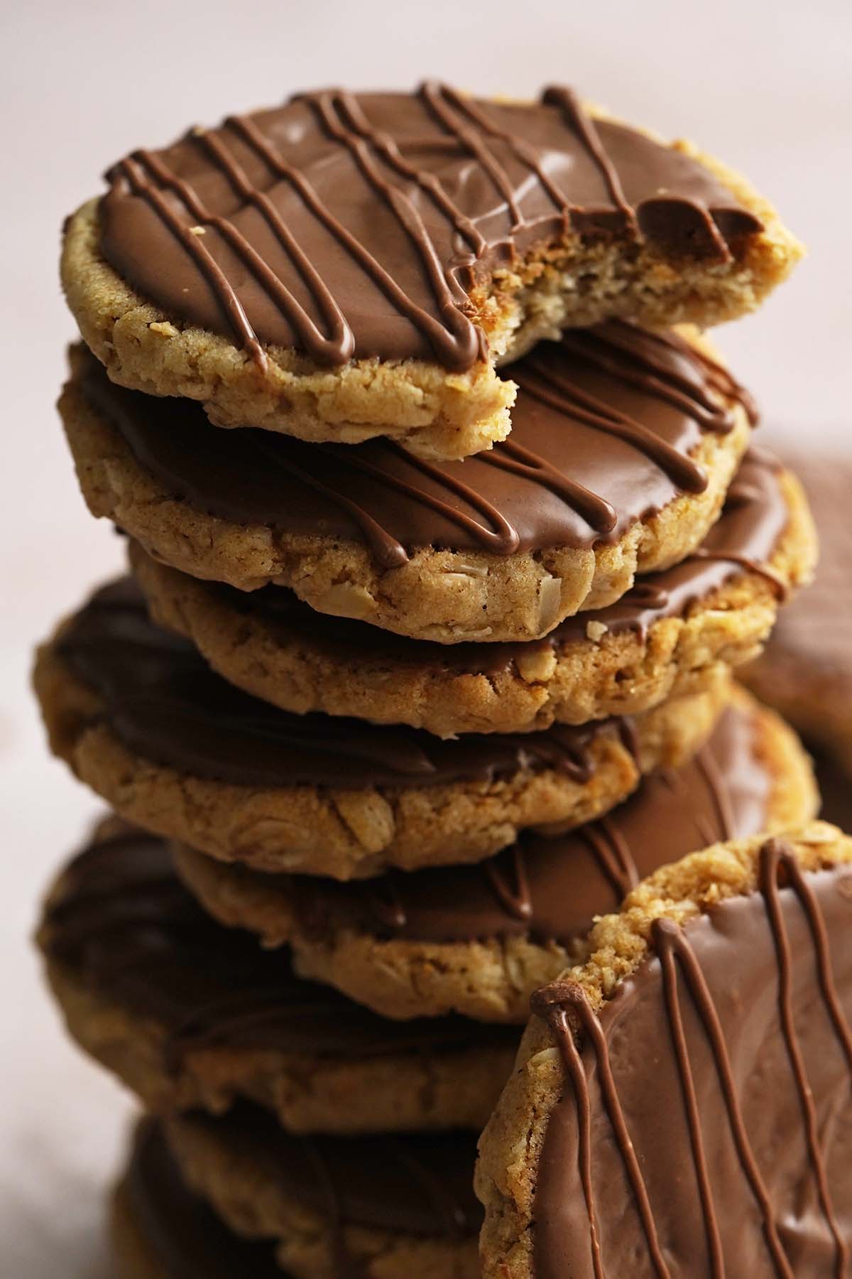 stack of crunchy oat cookies with chocolate topping with bite taken out of top cookie
