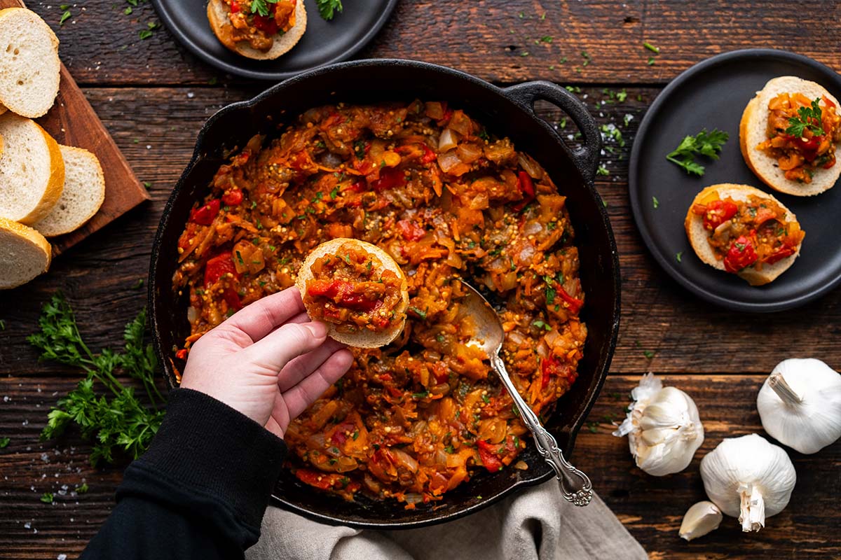 hand serving eggplant ikra on sliced bread